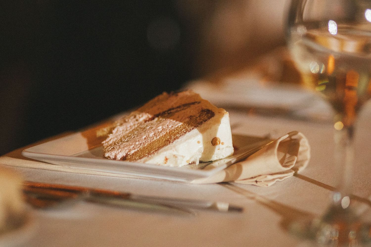 Elegant slice of tiramisu dessert on white plate at wedding reception table.