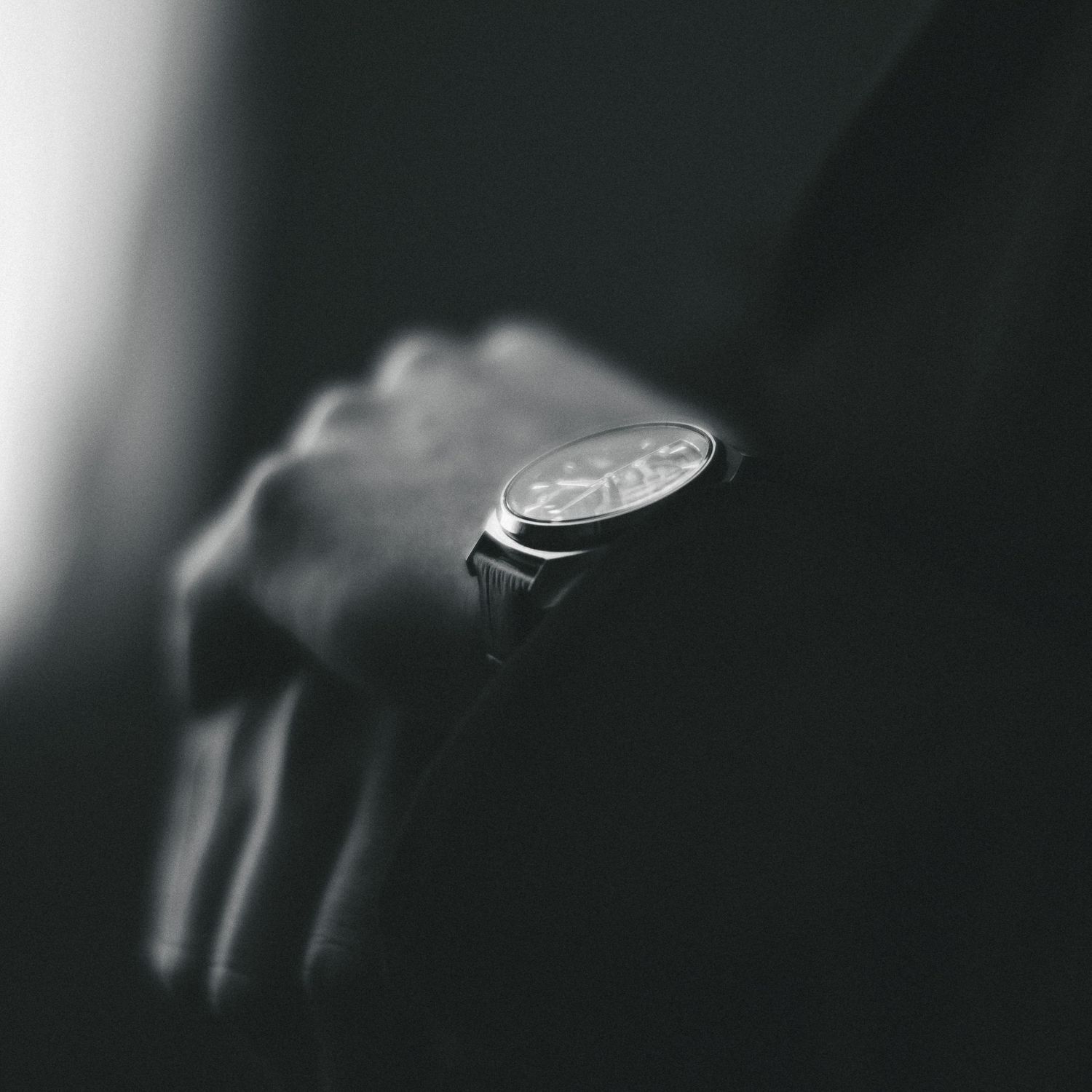 Close-up black and white photo of a man wearing an elegant analog wristwatch with a detailed dial.