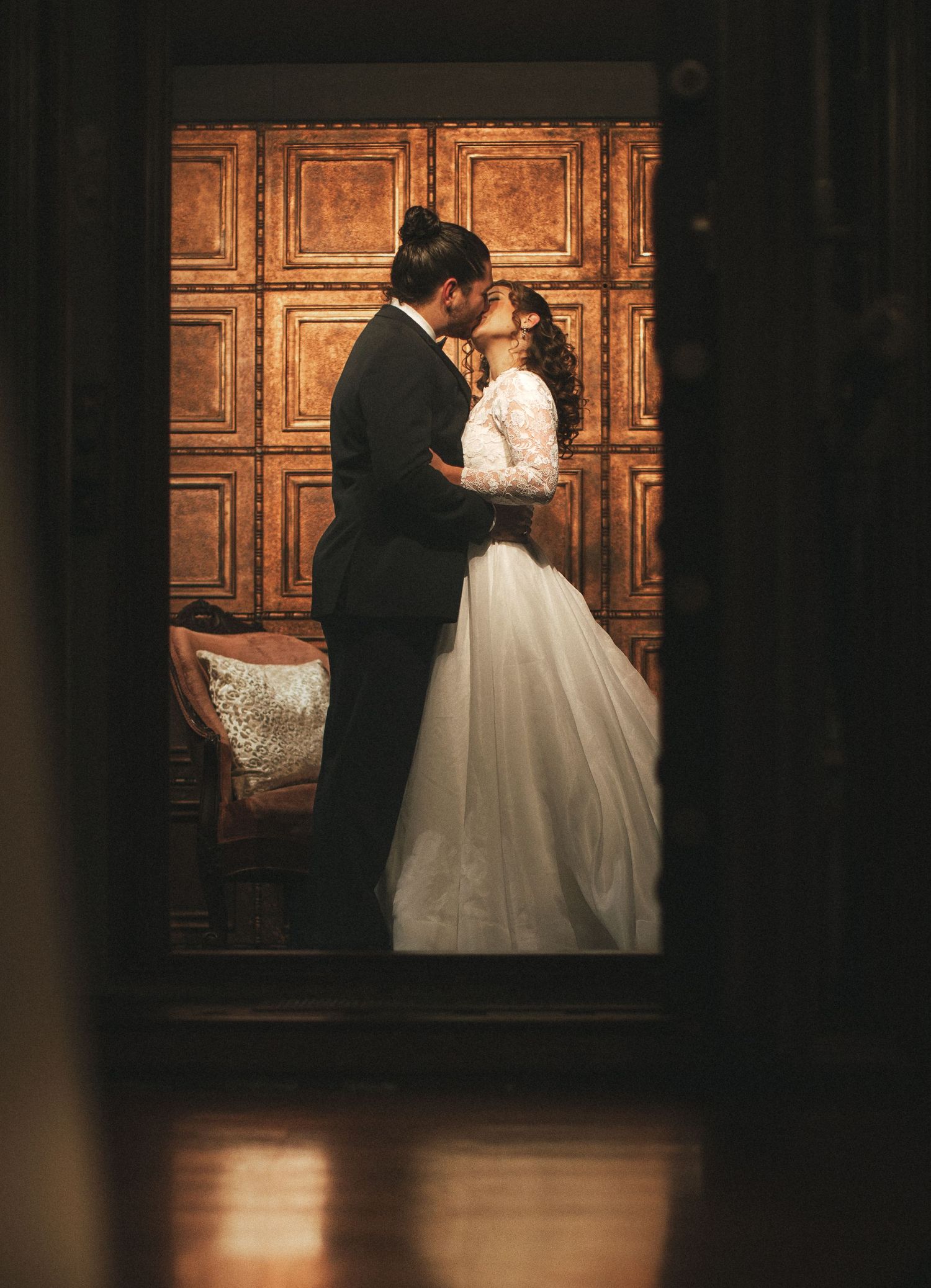 Bride and groom sharing a romantic kiss in elegant wood-paneled room, bride in white ballgown.