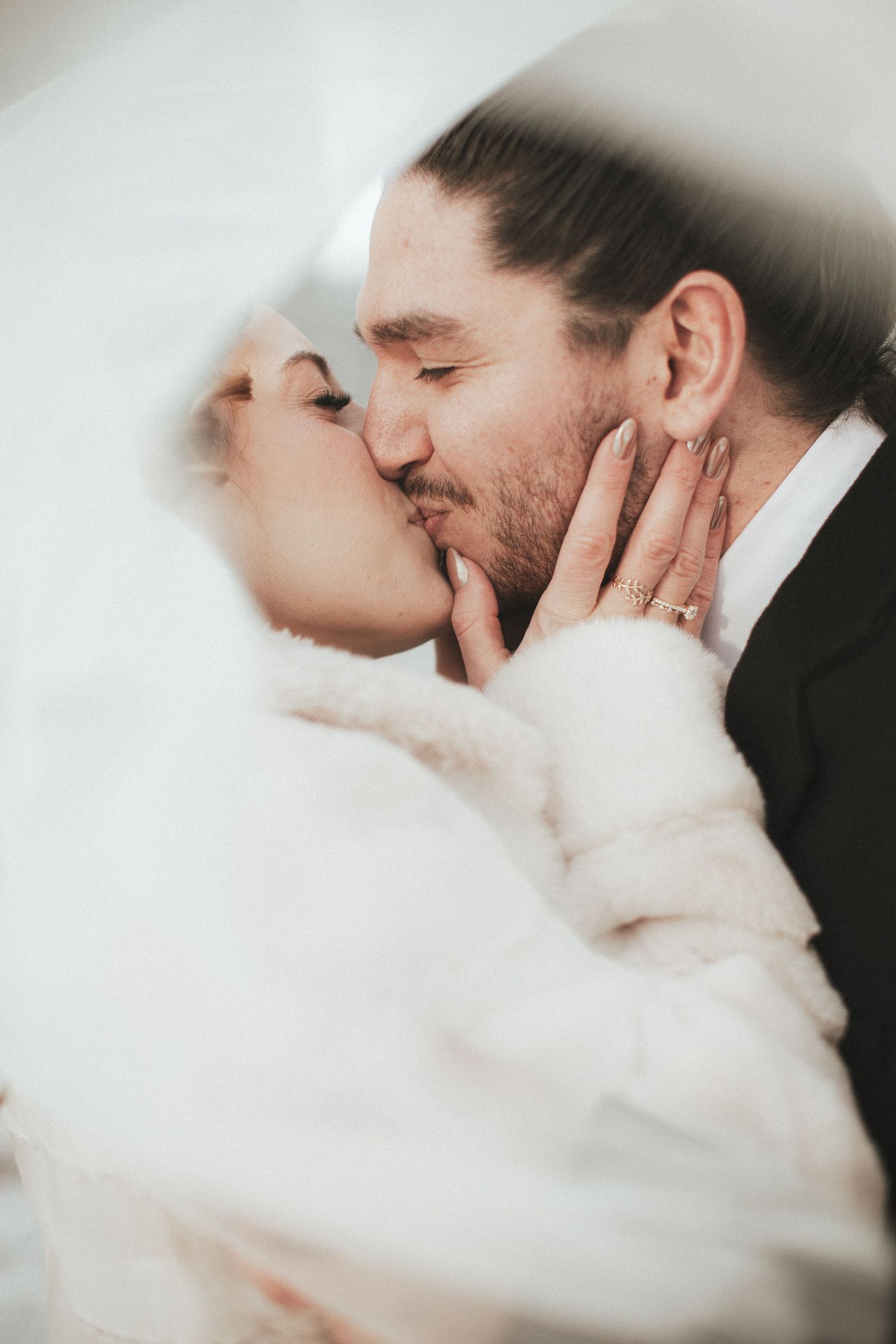 A bride and groom share a romantic kiss under a white veil on their wedding day.
