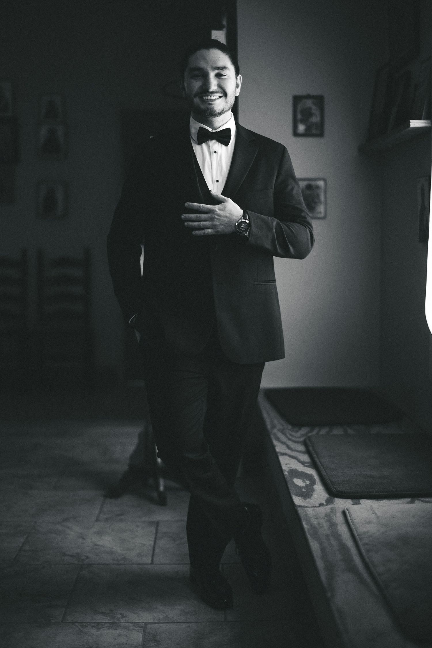 Black and white photo of smiling man in tuxedo with bow tie standing indoors.