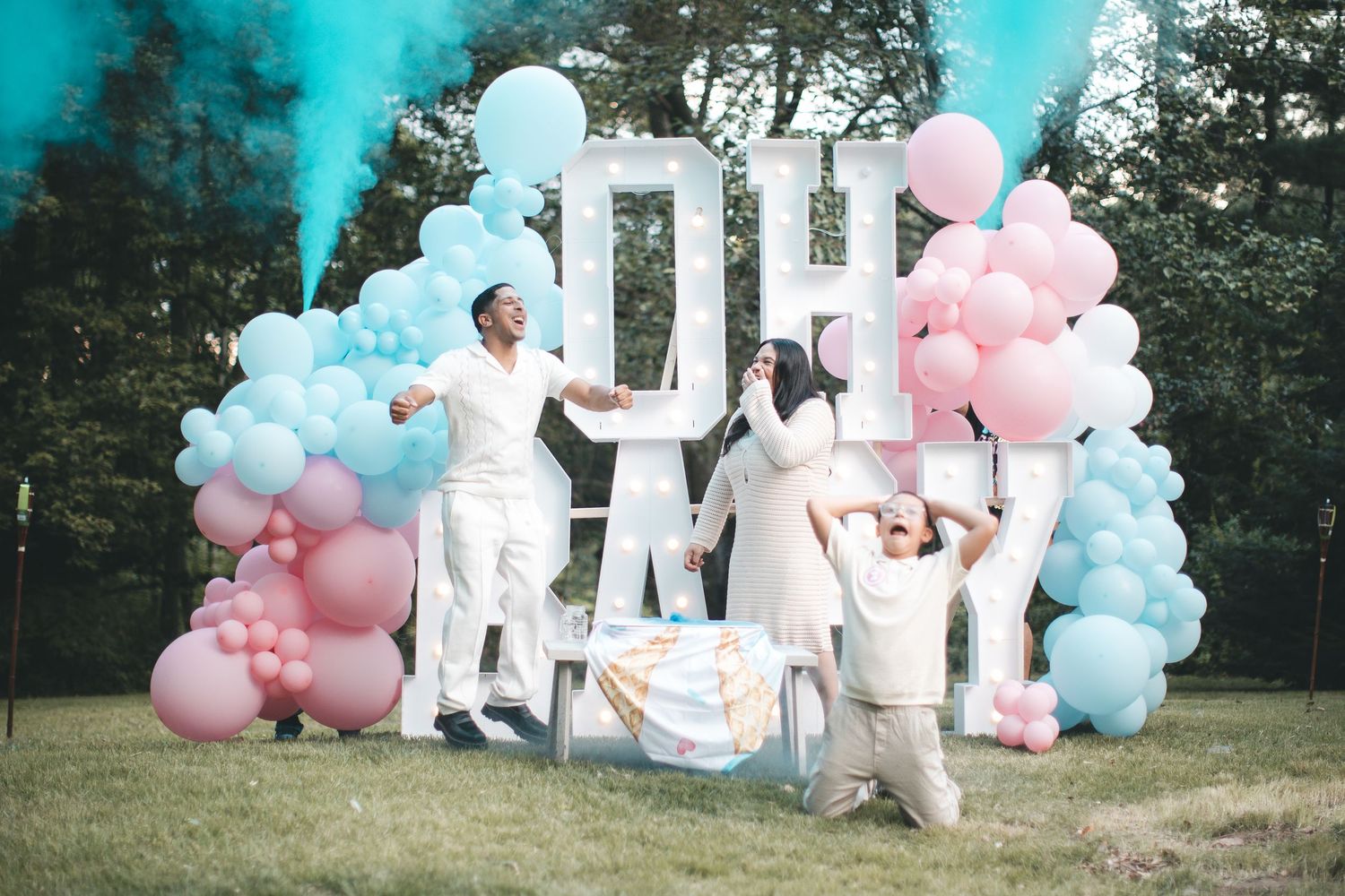 Gender reveal party with pink and blue balloons, smoke, and OH BABY letters outdoors.