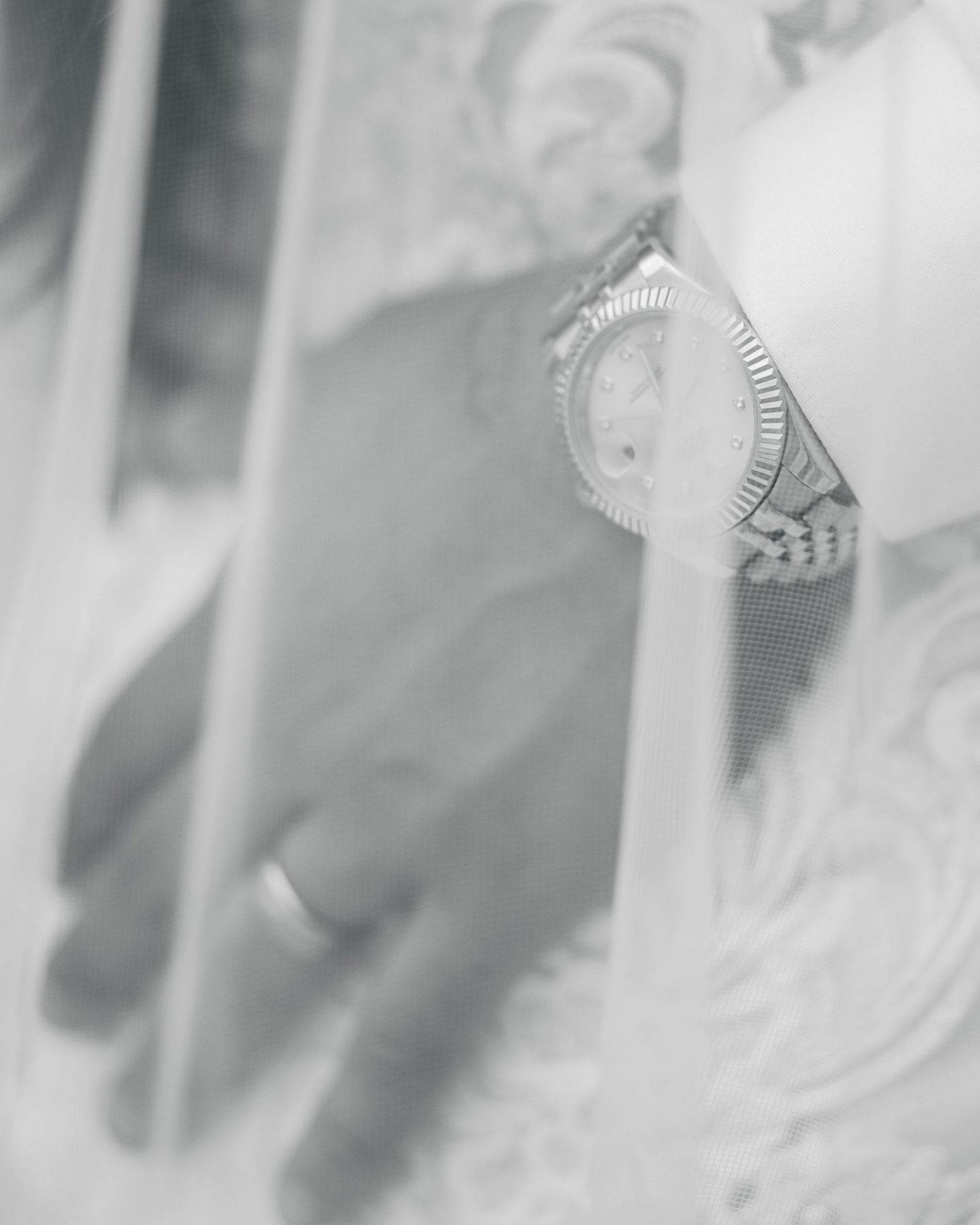 Black and white close-up of a hand wearing a Rolex watch and ring, holding a mirror.