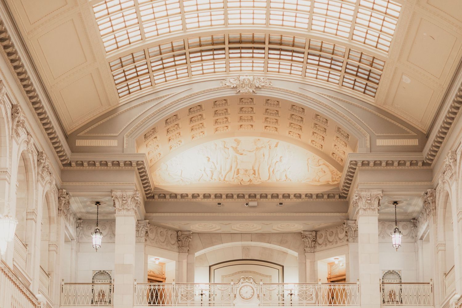 Ornate beaux-arts building interior with gilded arched ceiling, skylight, decorative moldings, and elegant chandeliers.