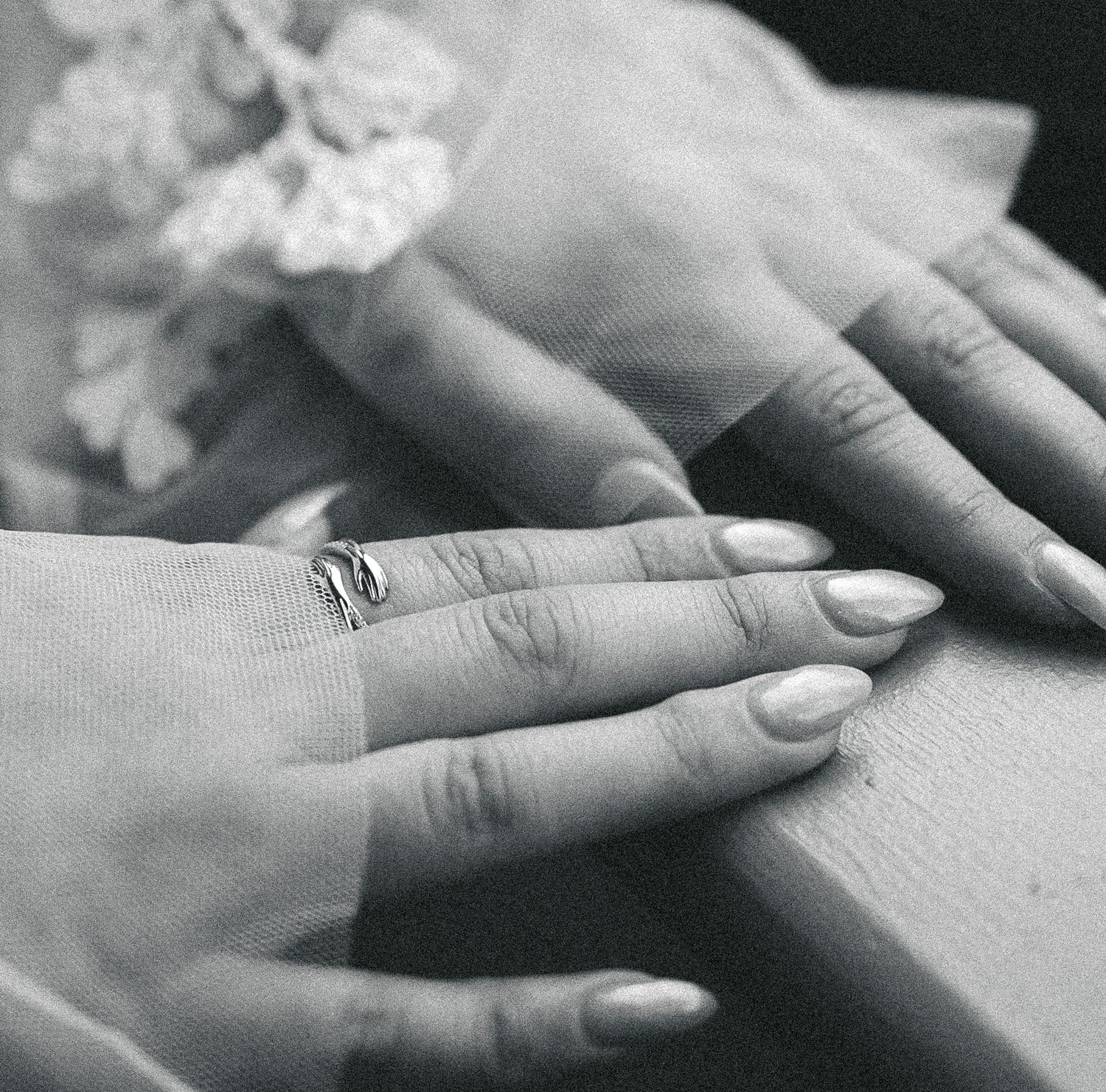 Black and white close-up of two hands with manicured nails and a delicate ring.