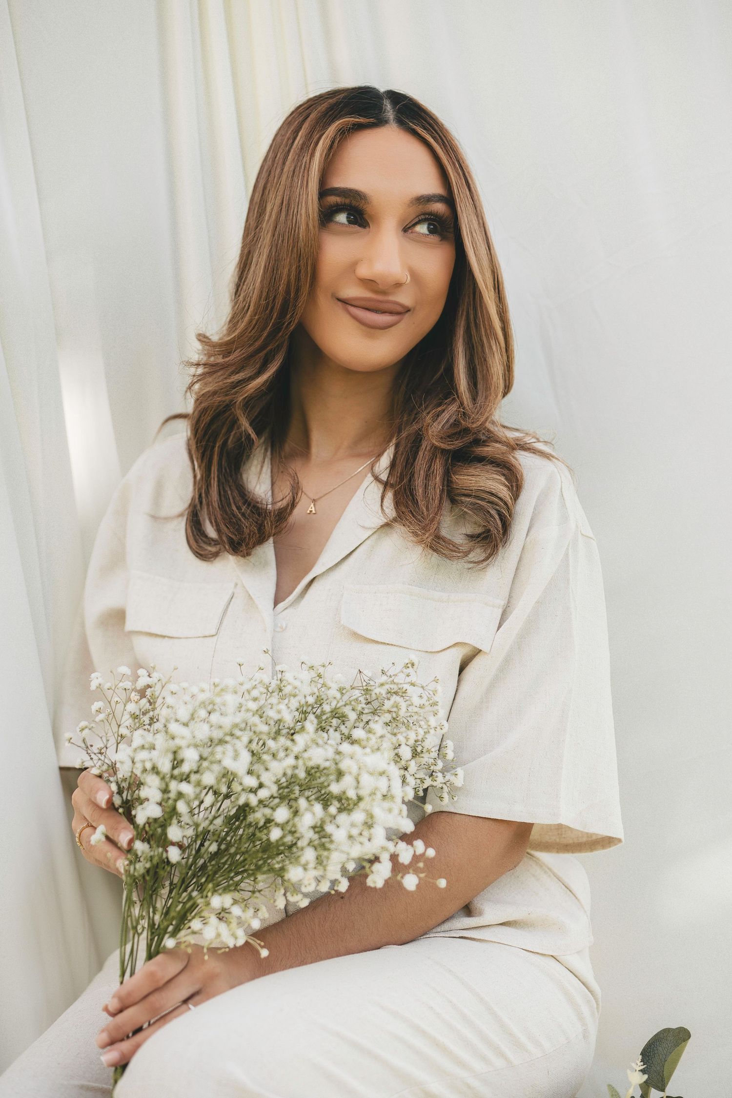 Woman in cream outfit holding white baby's breath flowers, posing elegantly for a bridal portrait.
