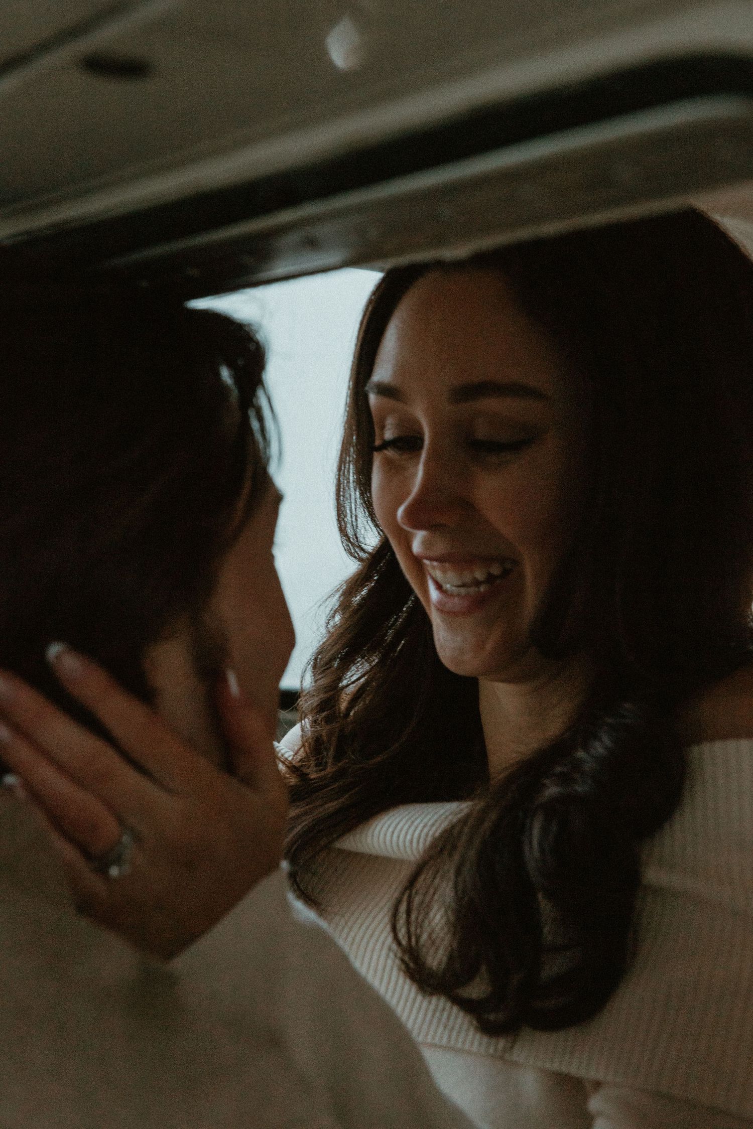 Smiling woman with dark hair embraces her partner closely inside a cozy vehicle interior.