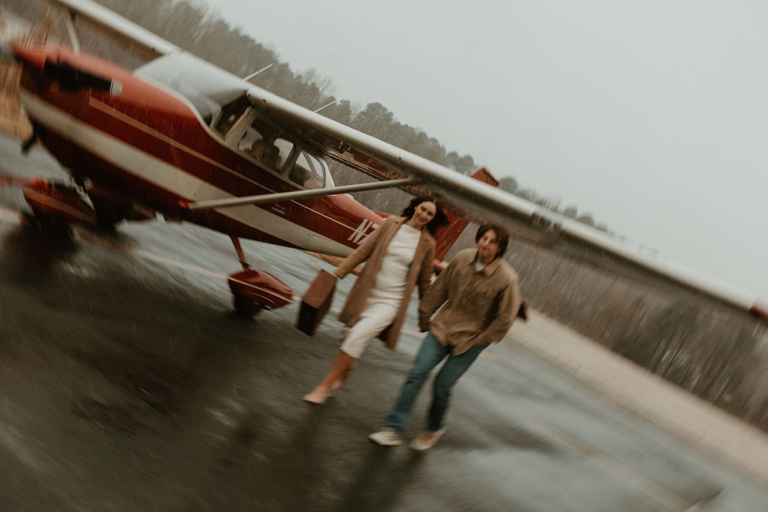 Couple walking together in front of vintage red airplane on airstrip.