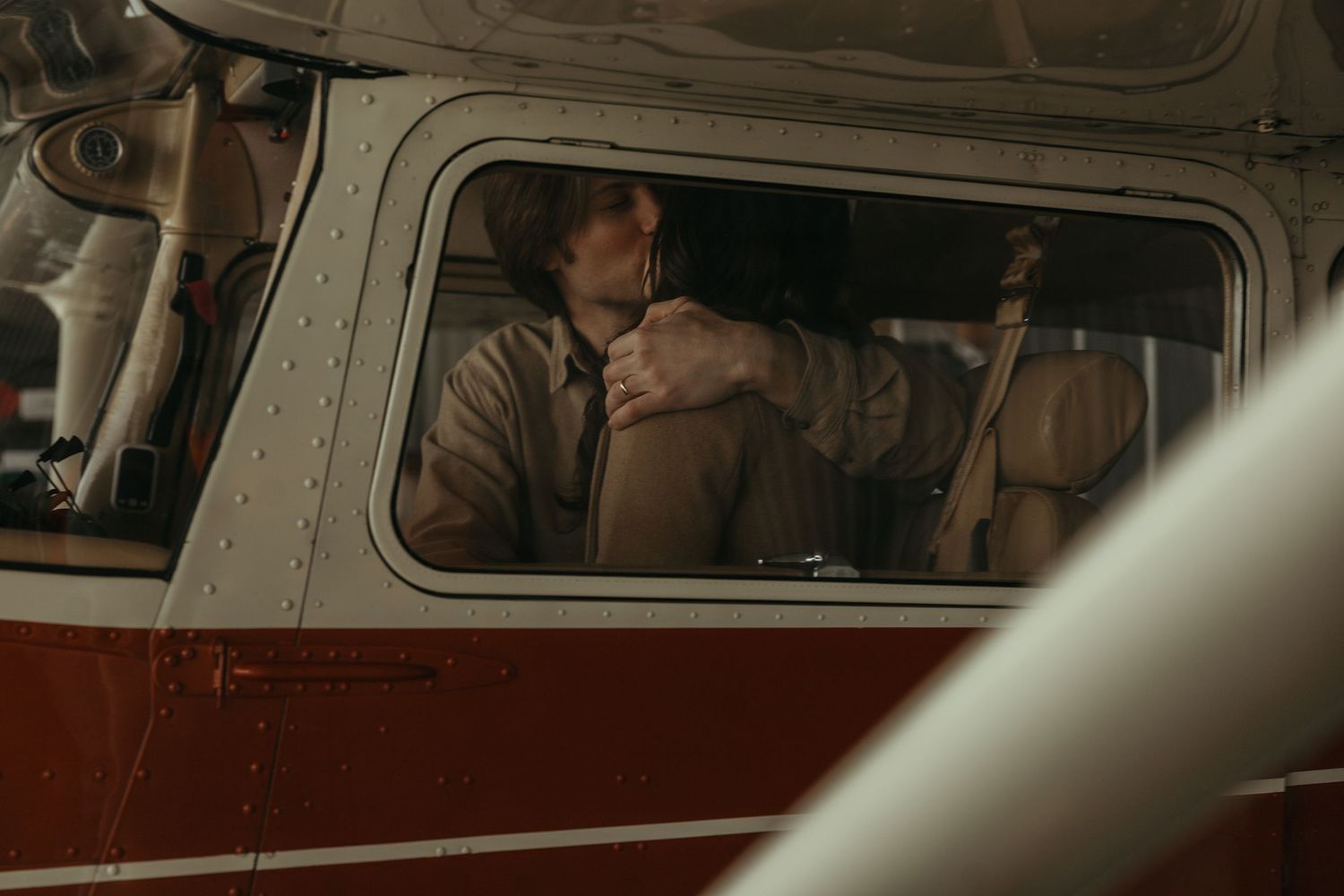 Person sitting alone inside a vintage red and white airplane, gazing thoughtfully out the window.