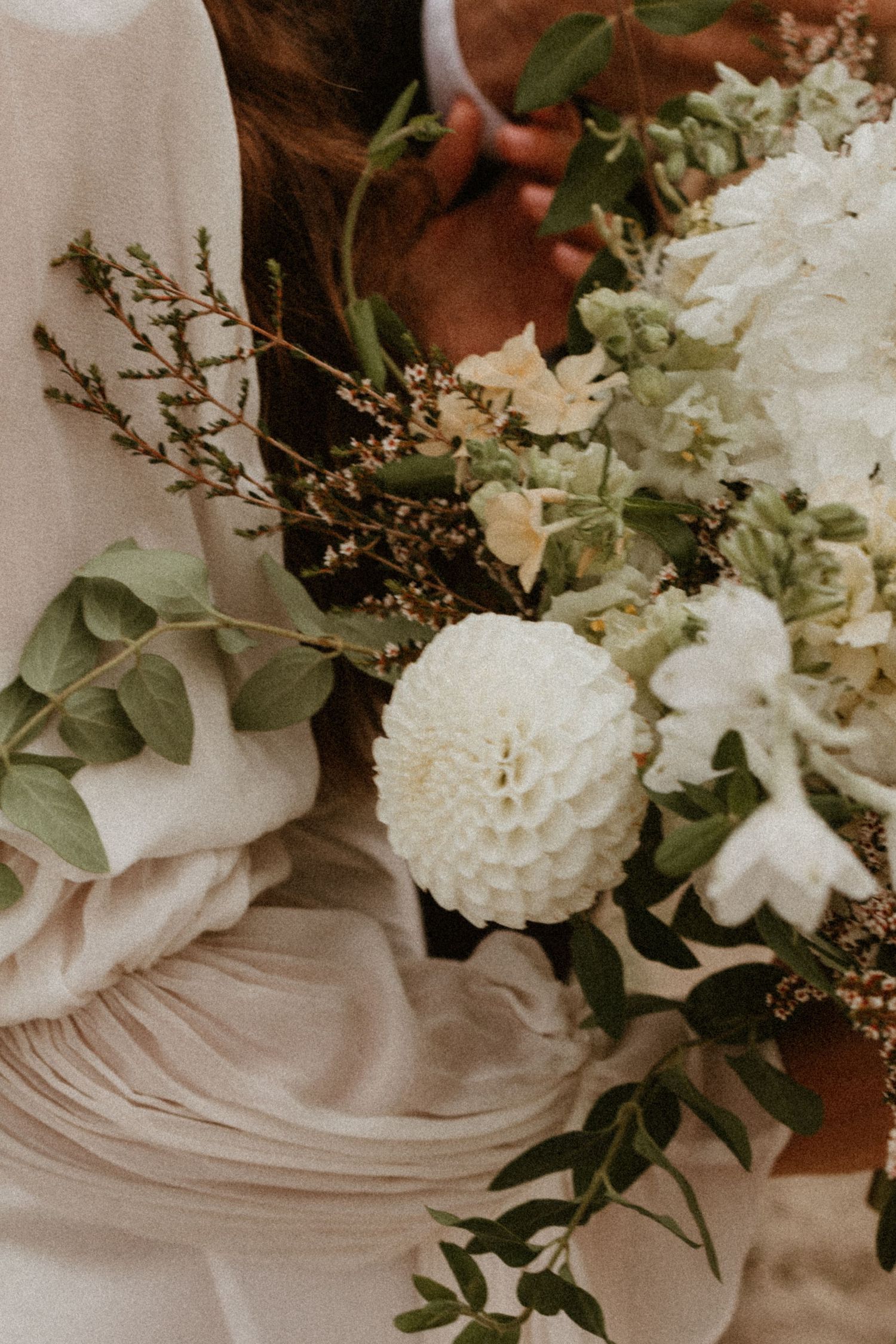 Close-up of a bridal bouquet featuring white dahlias, greenery, and delicate wildflowers.