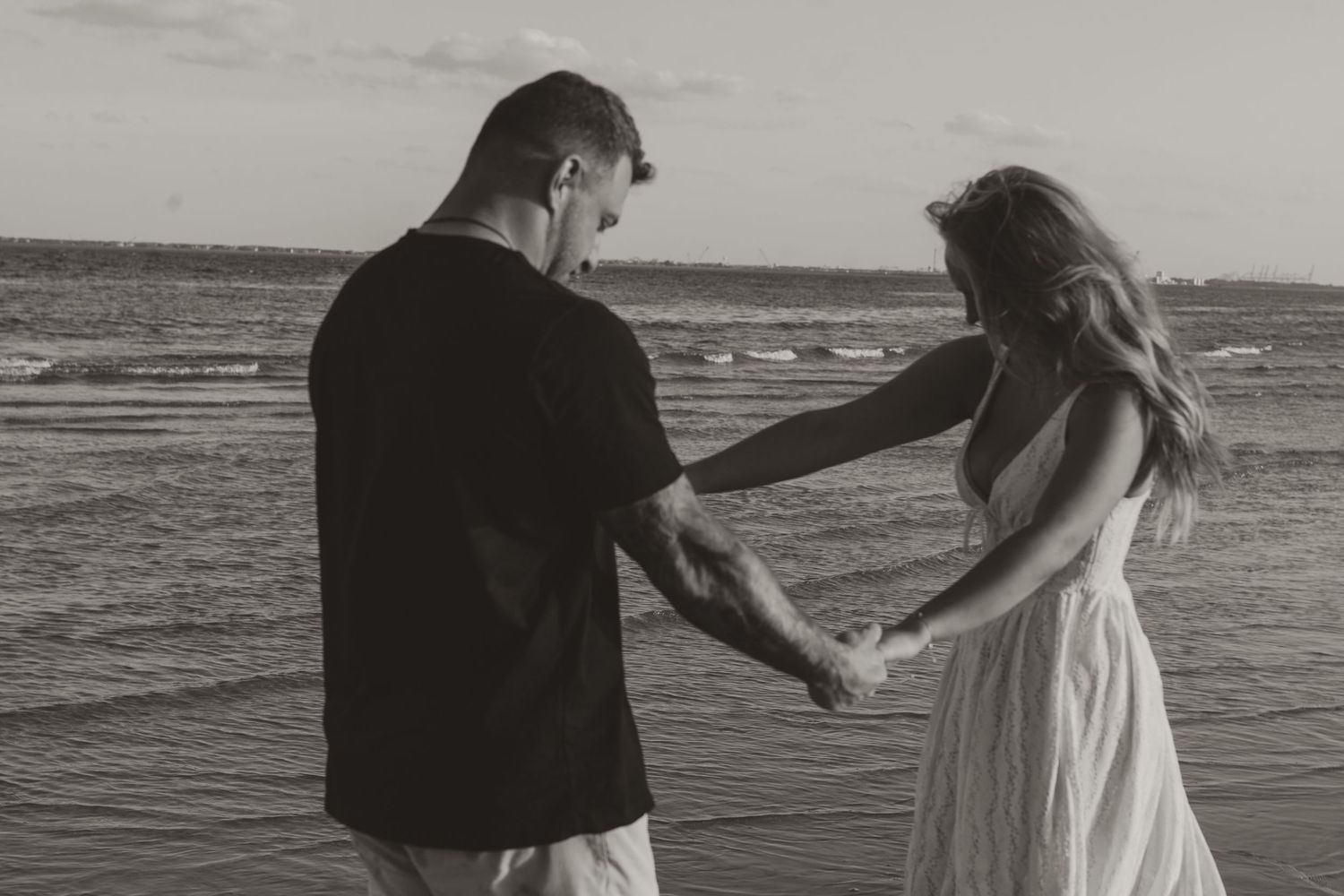 Couple holding hands on beach shore in black and white romantic photo.