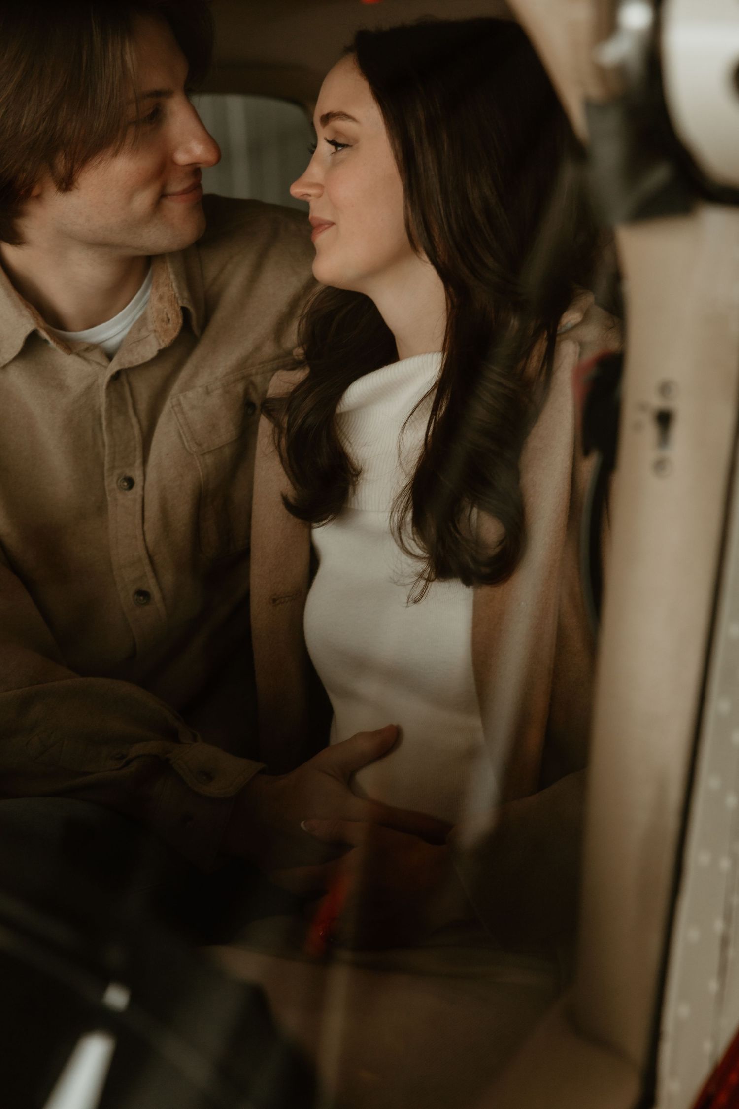 Couple sharing an intimate moment inside a vintage small aircraft, gazing lovingly at each other.