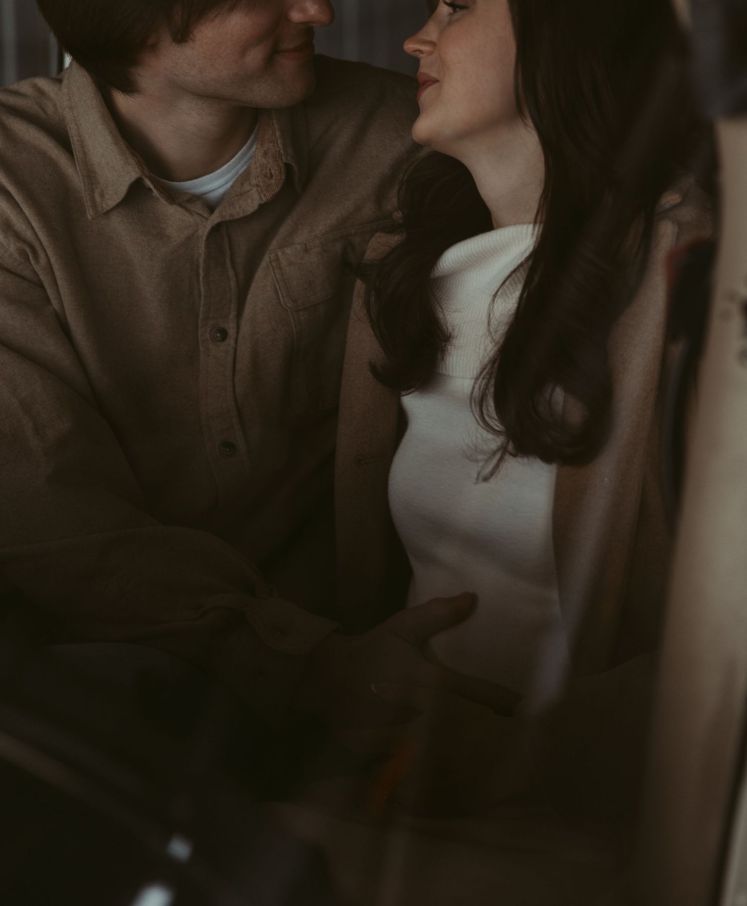 Couple sharing a close romantic moment, woman in white dress and man in brown shirt smiling.