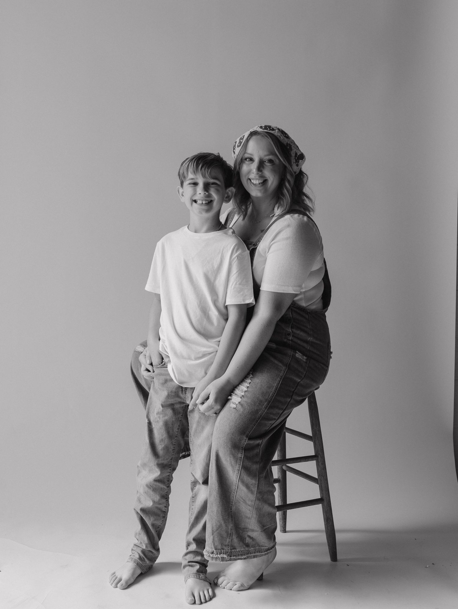 Black and white studio portrait of a smiling woman sitting on a stool with a young boy standing beside her.