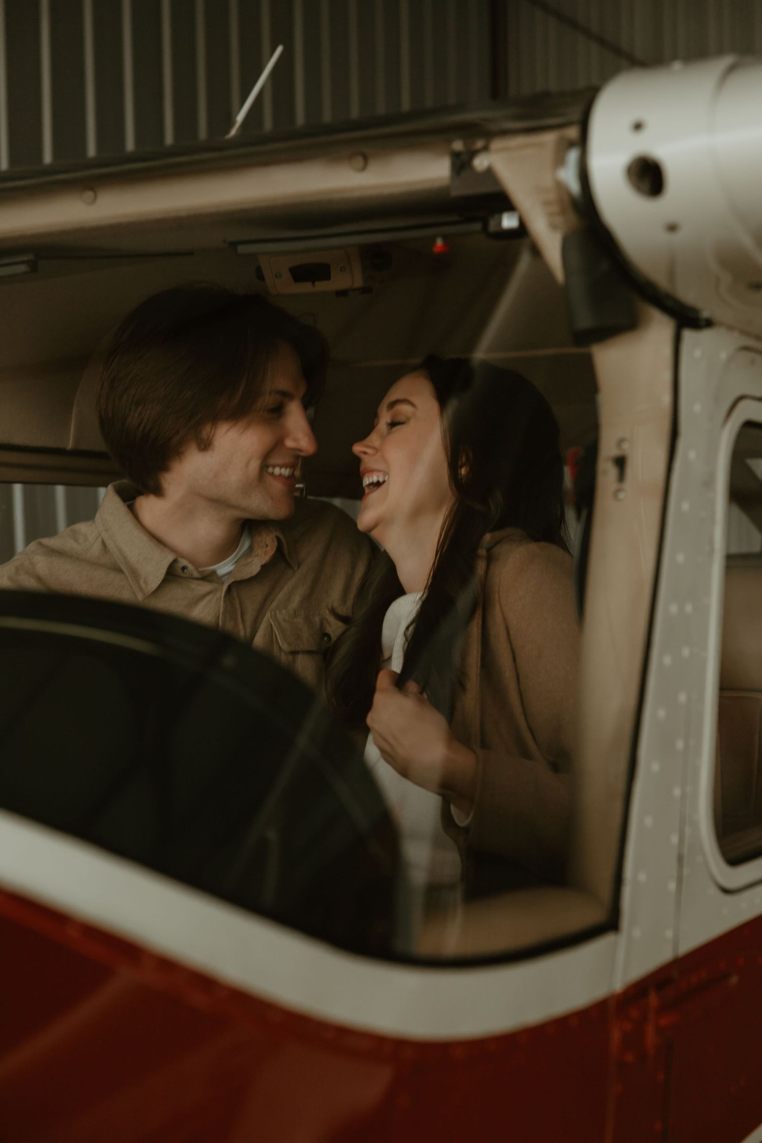 Happy laughing couple sitting together inside a vintage red and white small aircraft in a hangar.