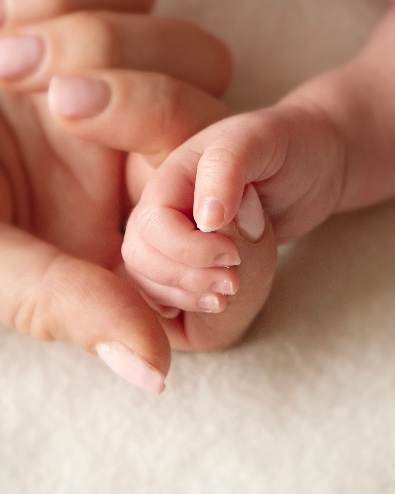 A newborn baby's tiny hand gently gripping an adult's finger on a soft white blanket.