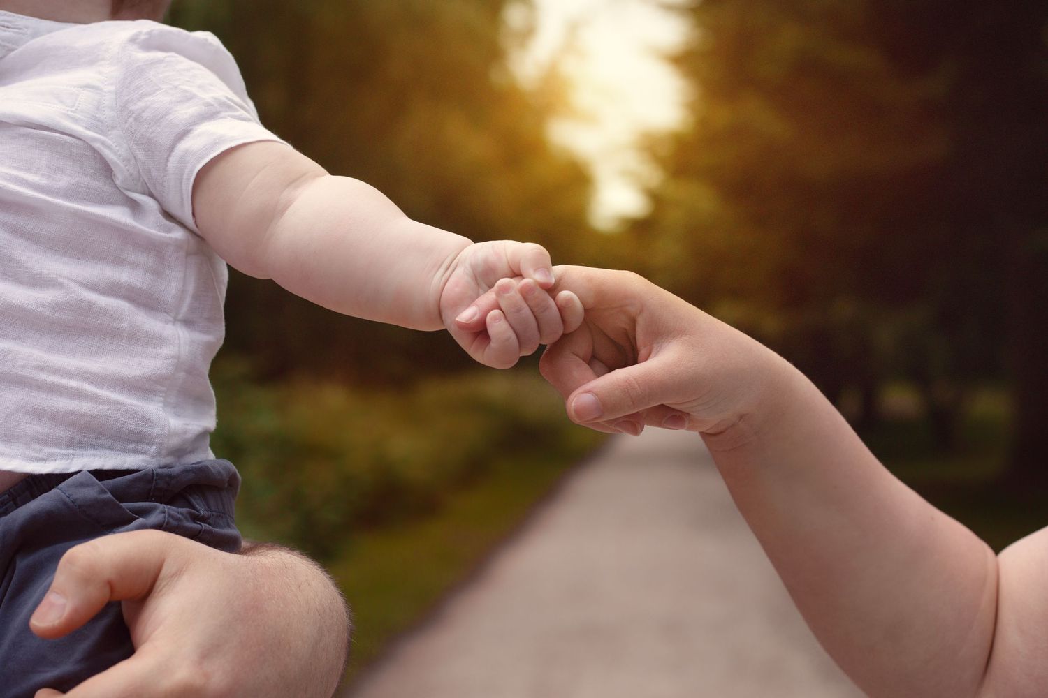 Baby reaching out to hold parent's finger on sunny outdoor path  in Birmingham