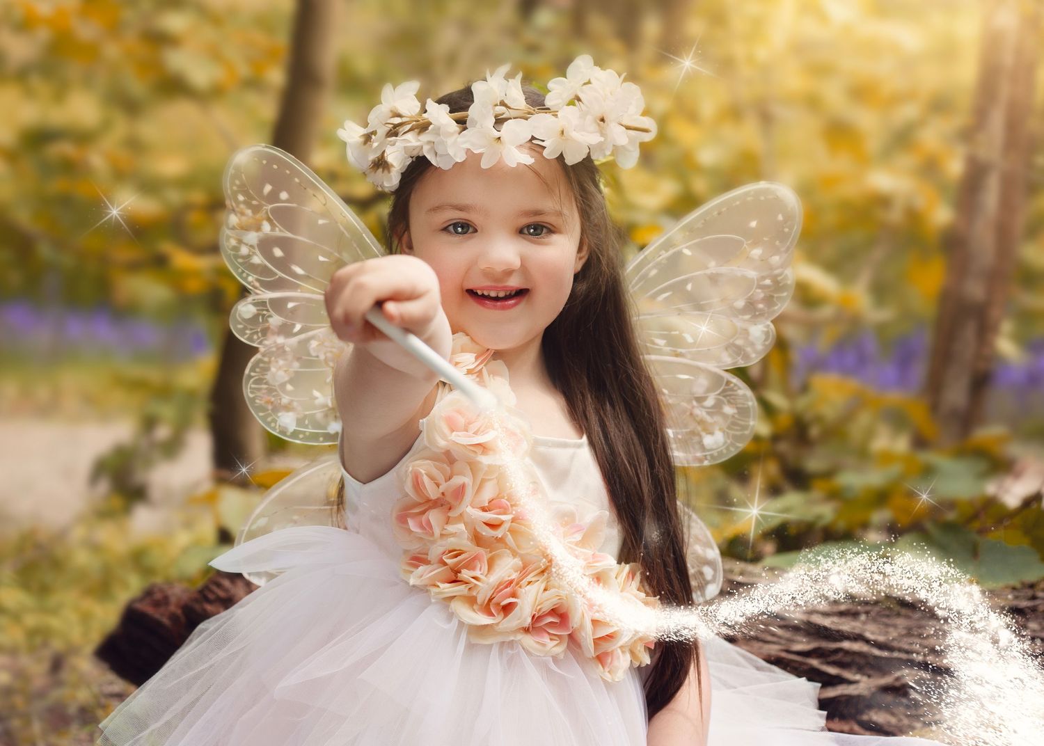 Smiling little girl dressed as fairy with butterfly wings and wand in sunlit autumn forest setting in Birmingham