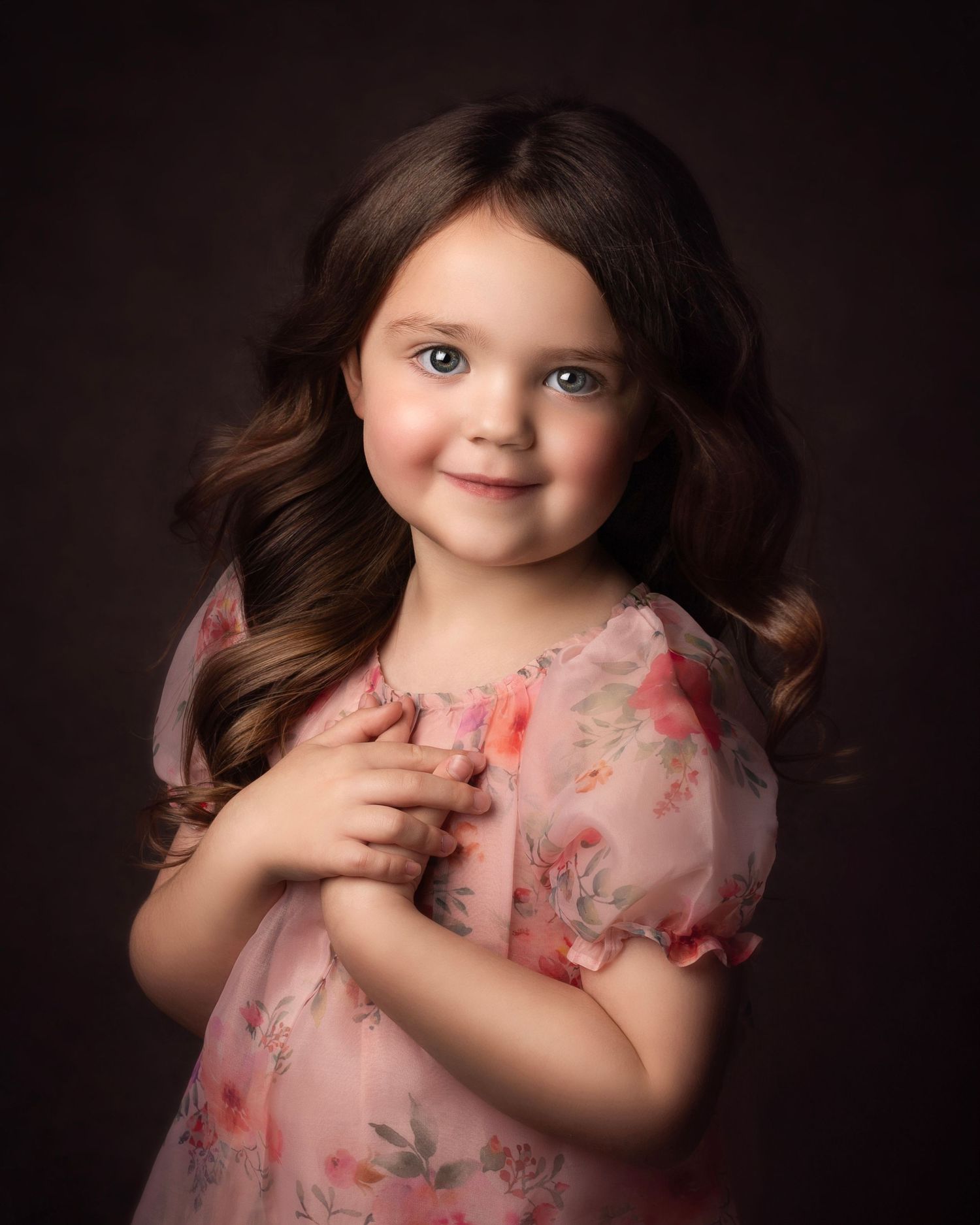Beautiful young girl with brown curly hair in a pink floral dress poses in a studio portrait  in Birmingham