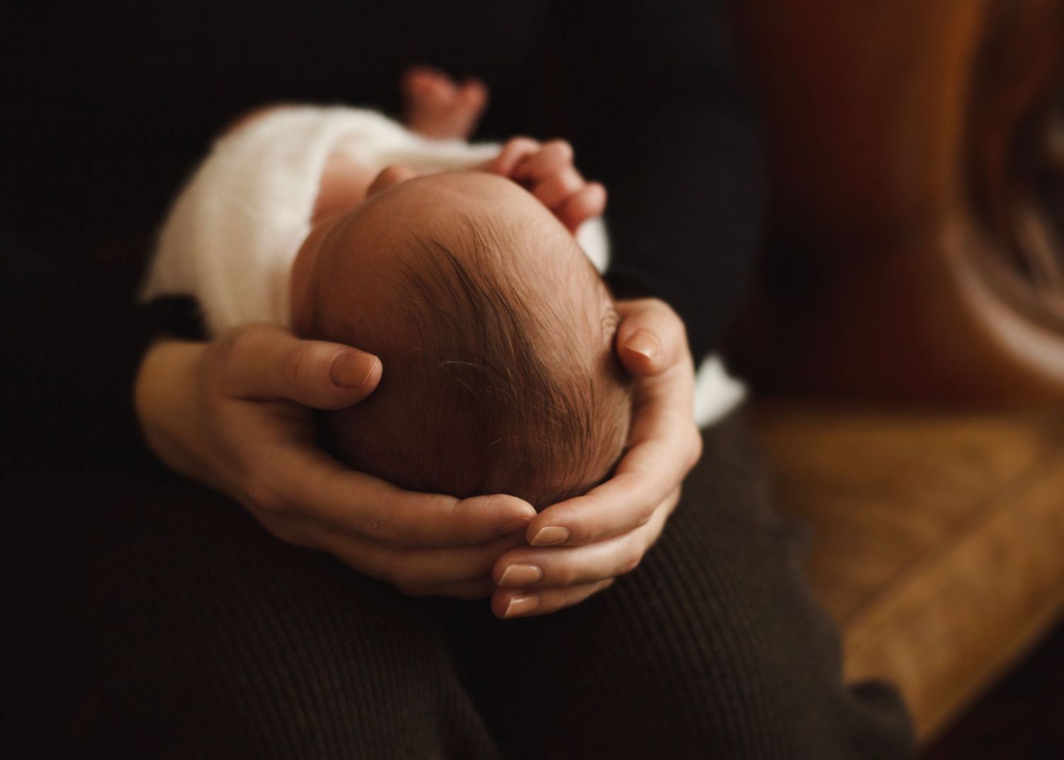 Parent gently cradling newborn baby's head in hands in warm light  in Birmingham