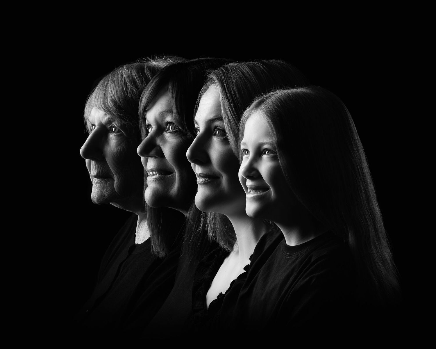 Black and white portrait of four generations of women posed in profile against a dark background  in Birmingham
