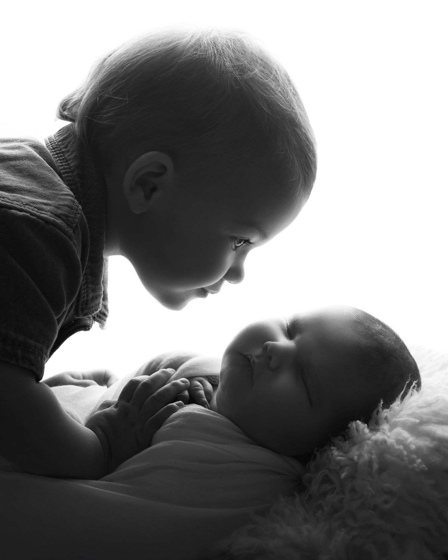 Black and white photo of young child gazing lovingly at sleeping newborn sibling in the West Midlands