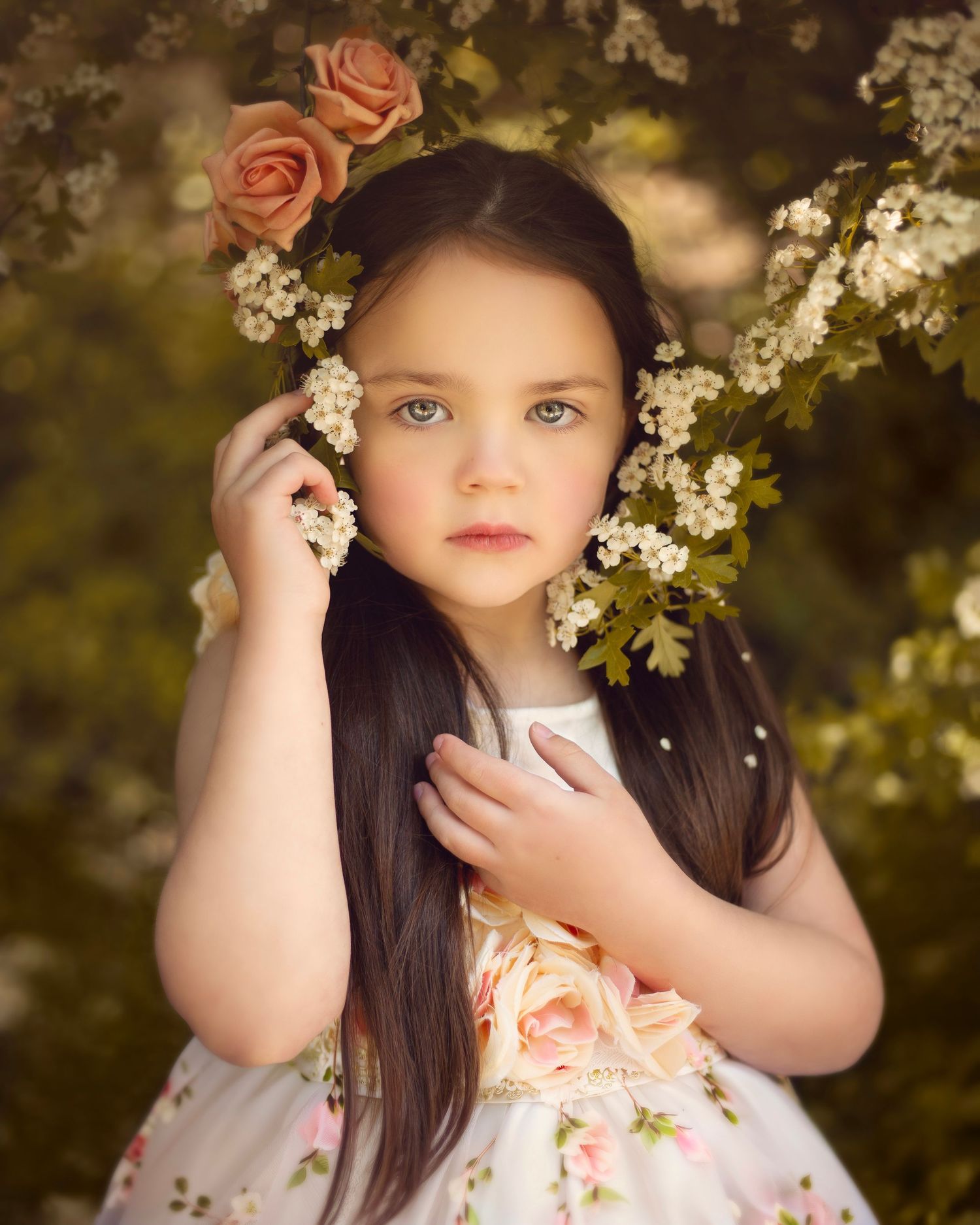 Beautiful young girl in floral dress posing among blooming pink roses and white spring blossoms outdoors in the West Midlands