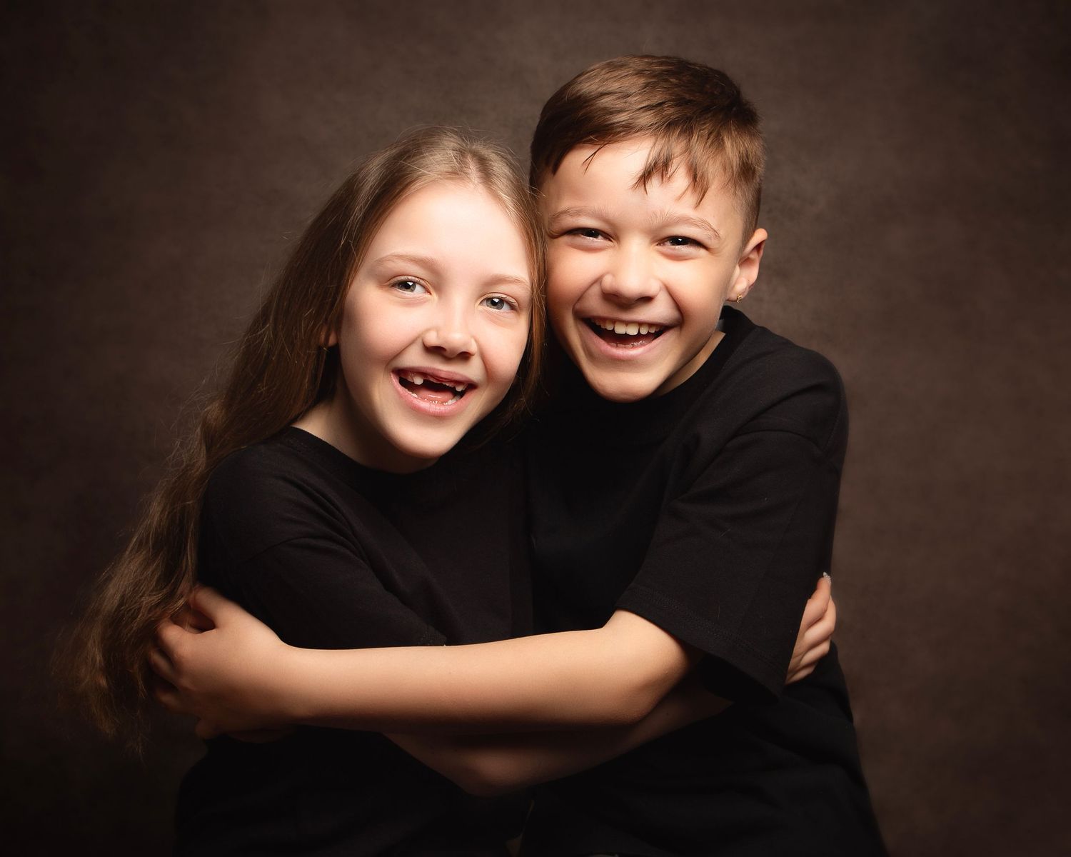 Two happy siblings in black shirts hugging and smiling in a warm studio portrait  in Birmingham