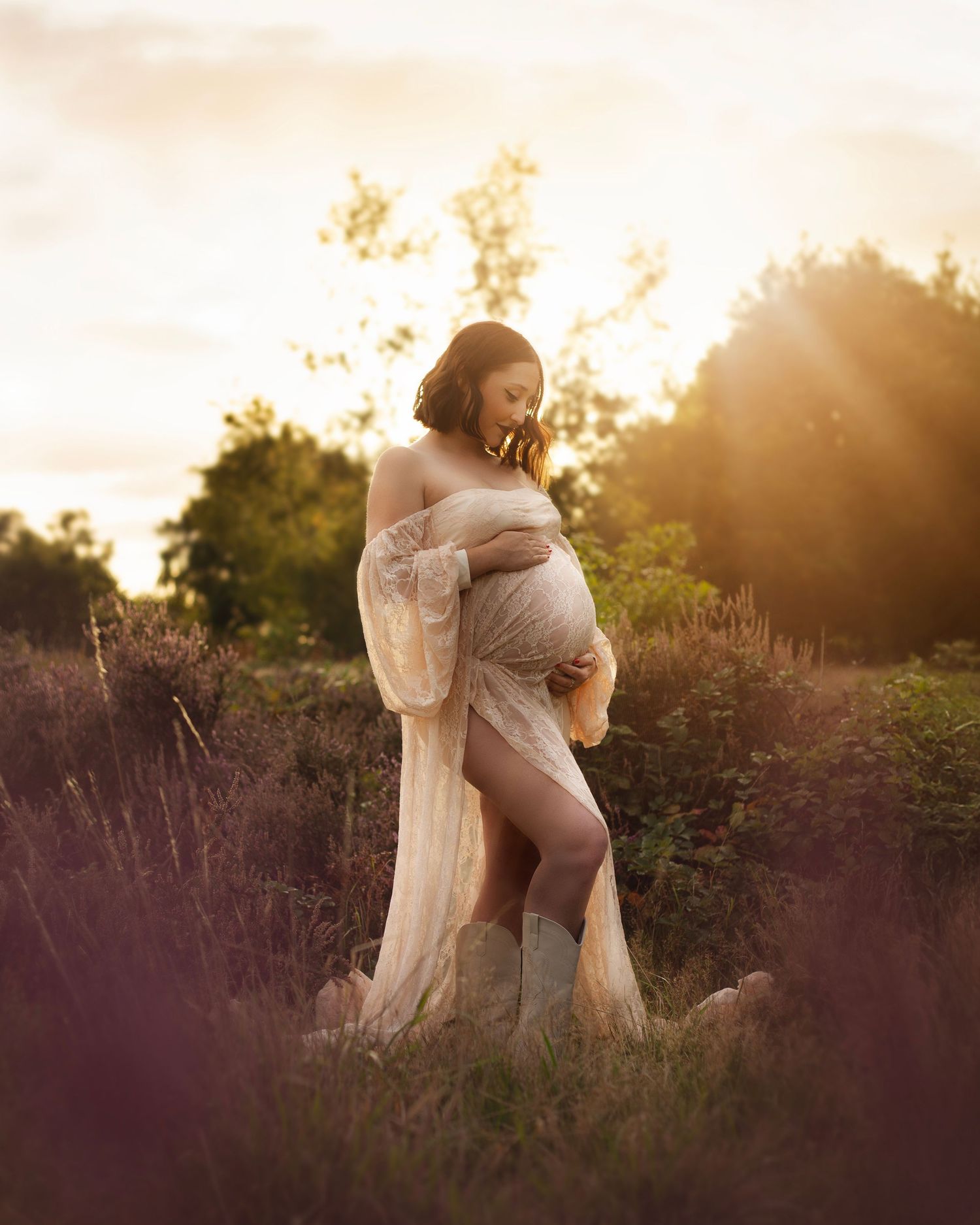 Pregnant woman in lace gown standing in heather field during golden hour sunset maternity shoot  in Birmingham