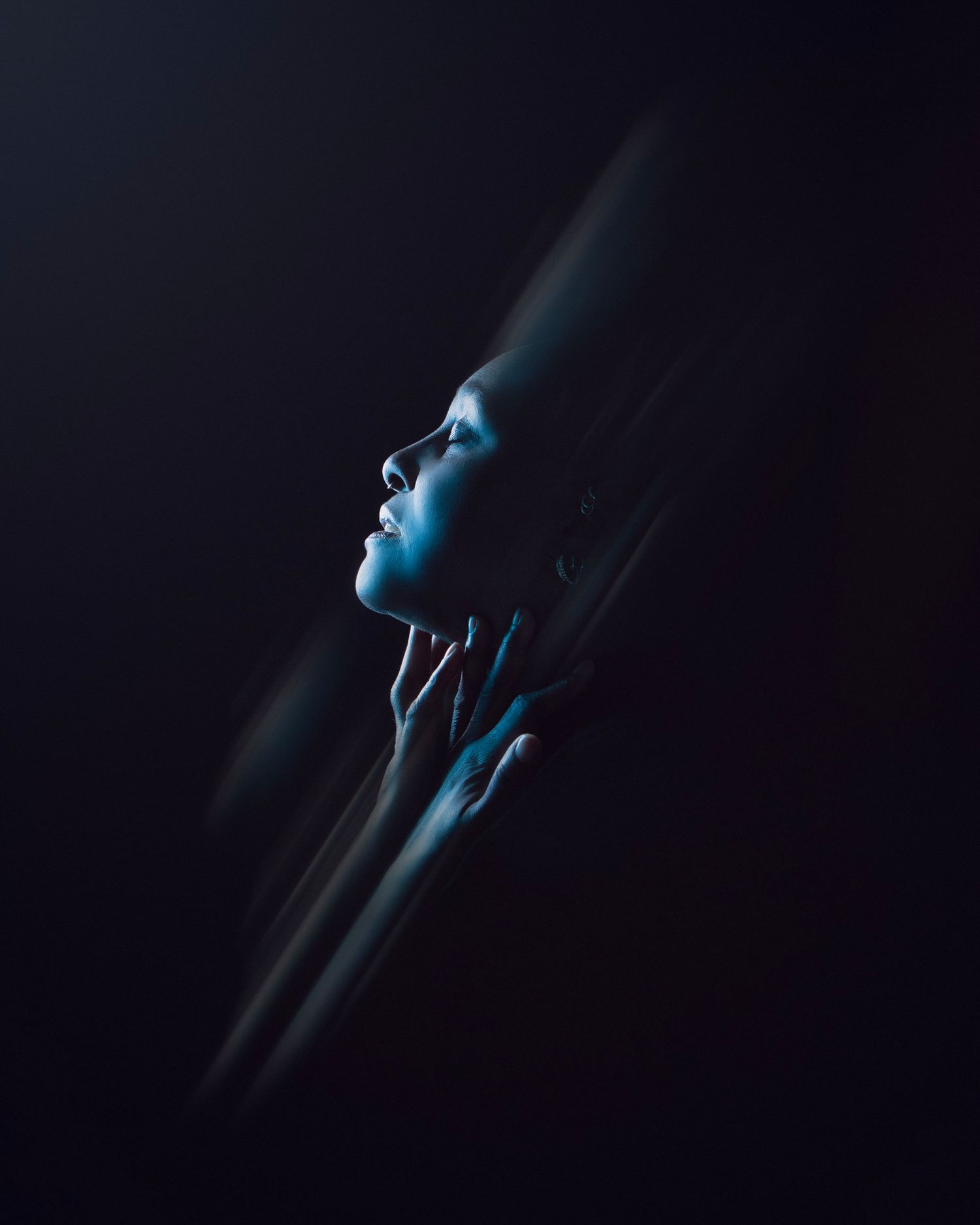 A woman's profile illuminated by blue light emerges from dark shadows in a dramatic fine art portrait, in Walsall