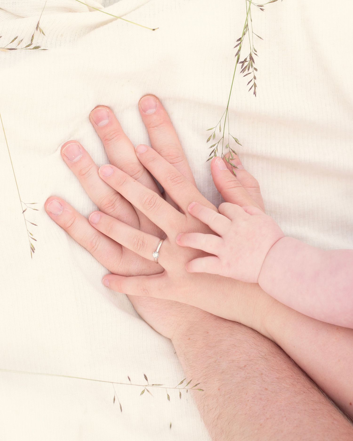 Three generations of hands resting together, showing a parent, adult, and baby hand with a wedding ring in the West Midlands