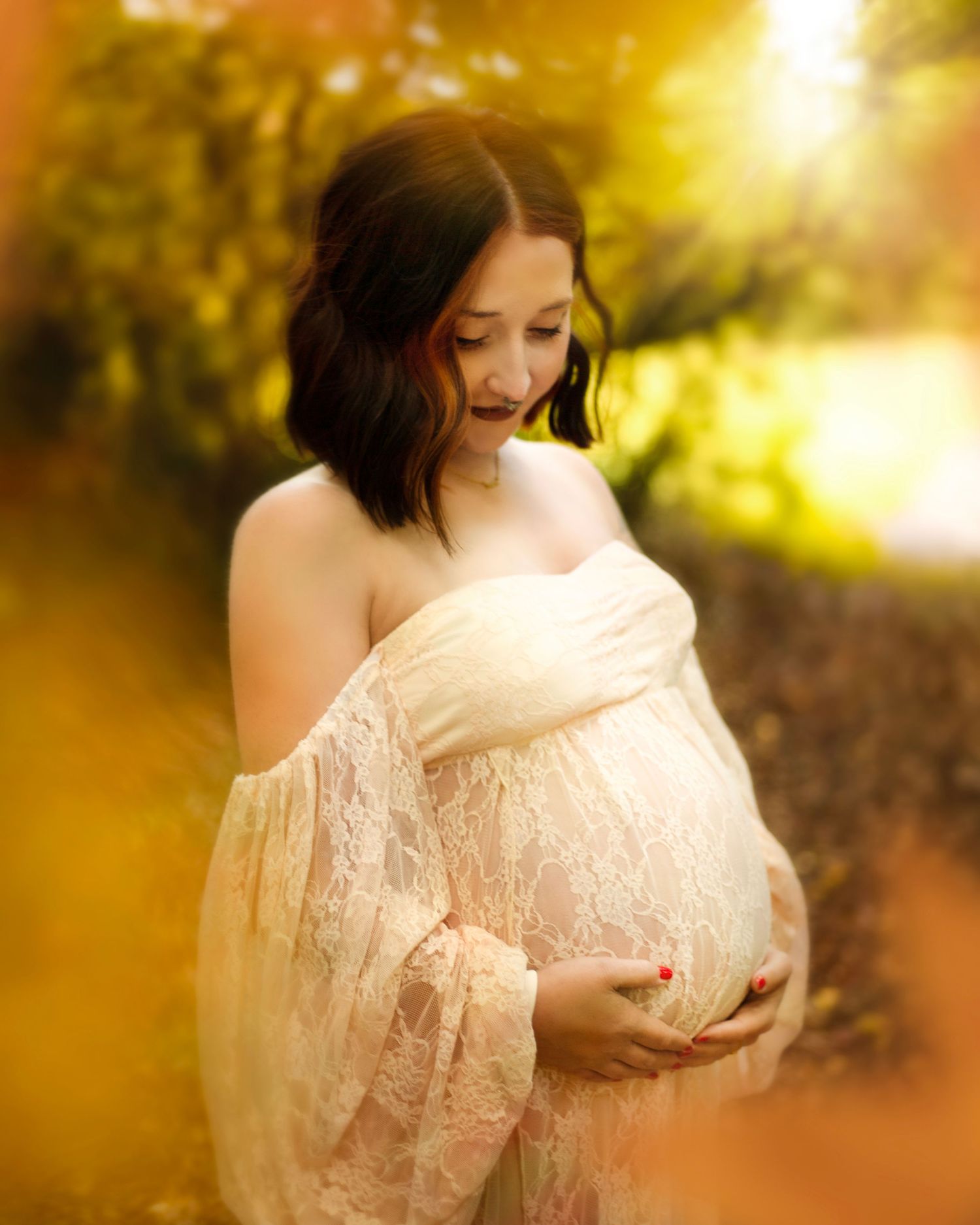 Pregnant woman in cream lace dress cradling baby bump surrounded by golden bokeh outdoor light in Birmingham