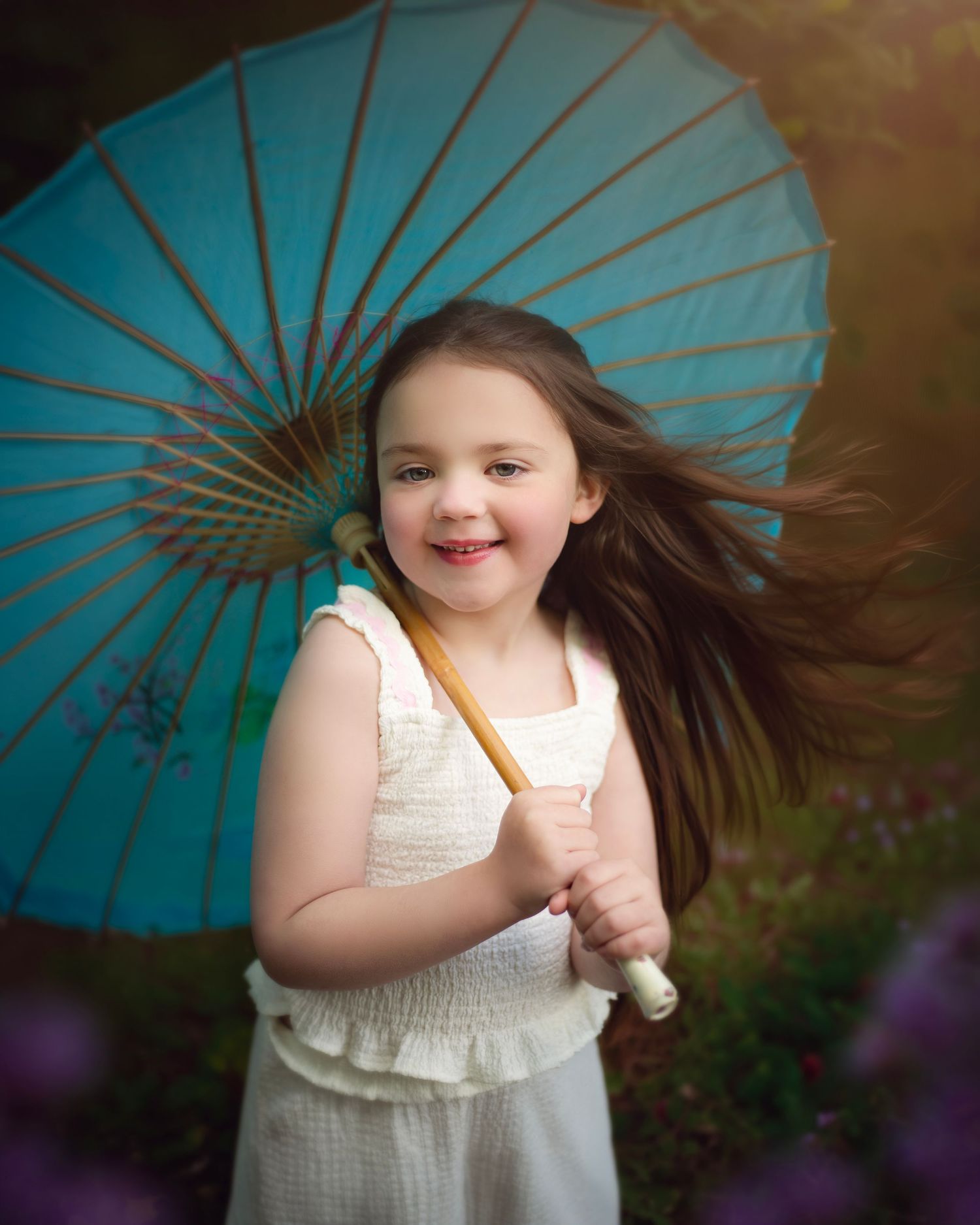 Young girl in white dress holds a teal parasol with hair blowing in a dreamy outdoor portrait, in the West Midlands