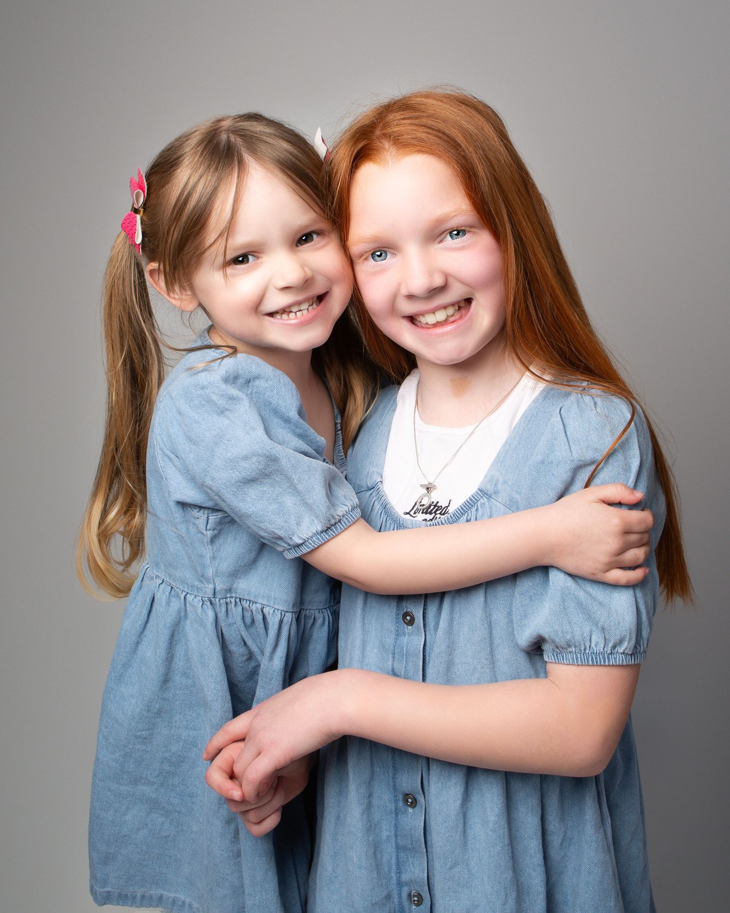 Two sisters in matching denim dresses smiling and embracing in professional studio portrait photo in the West Midlands