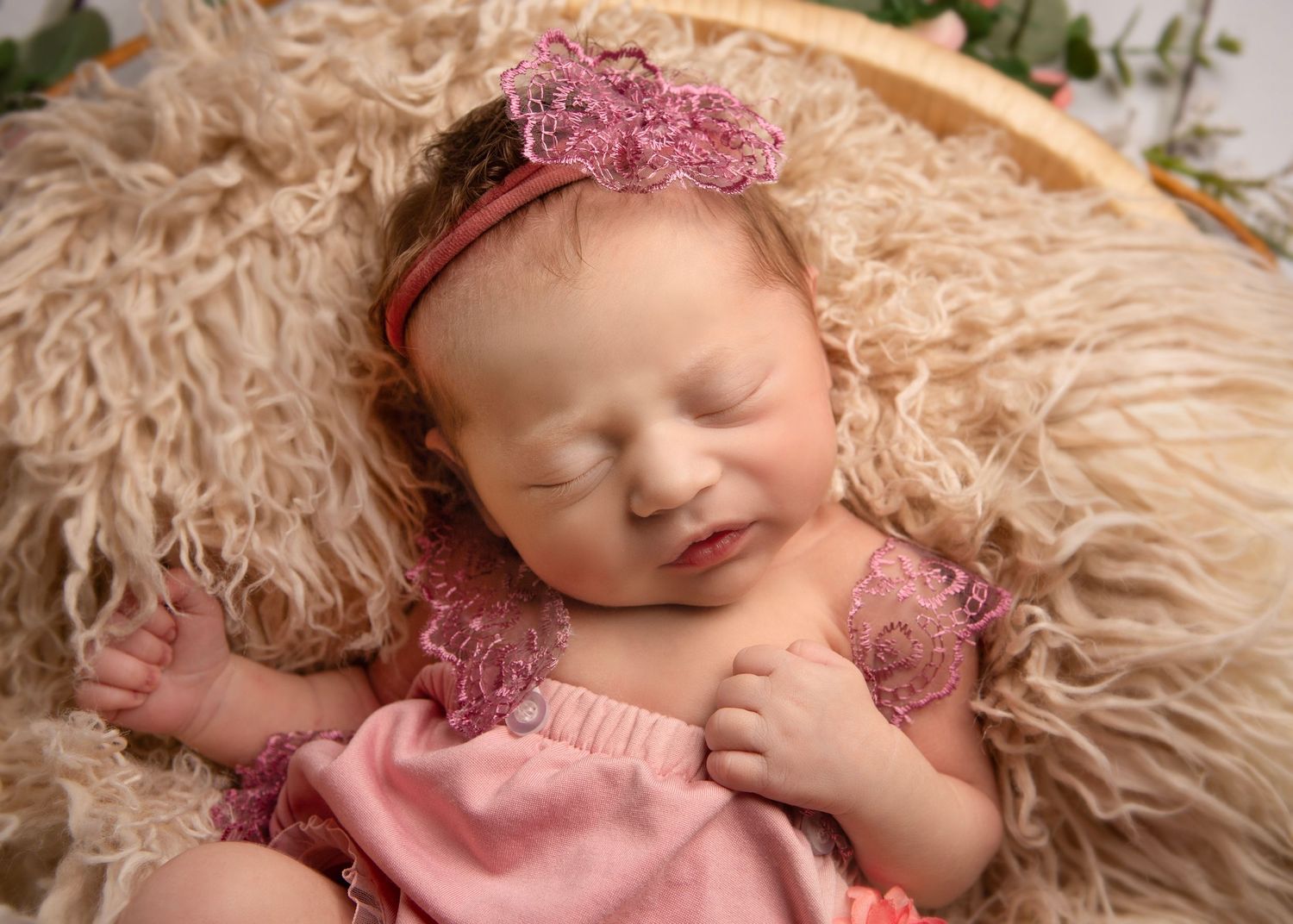Close-up of peacefully sleeping newborn in pink outfit with floral headband on soft cream fur in Wolverhampton