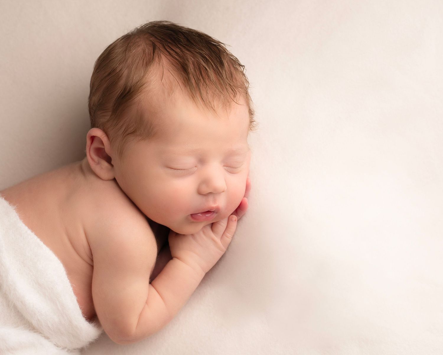 Peaceful sleeping newborn baby rests on white blanket with hands tucked under cheek  in Birmingham
