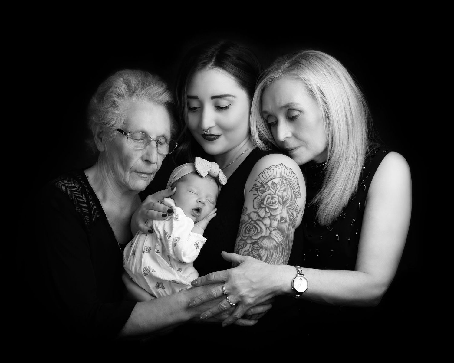 Black and white portrait of three generations of women lovingly holding a newborn baby girl in the West Midlands