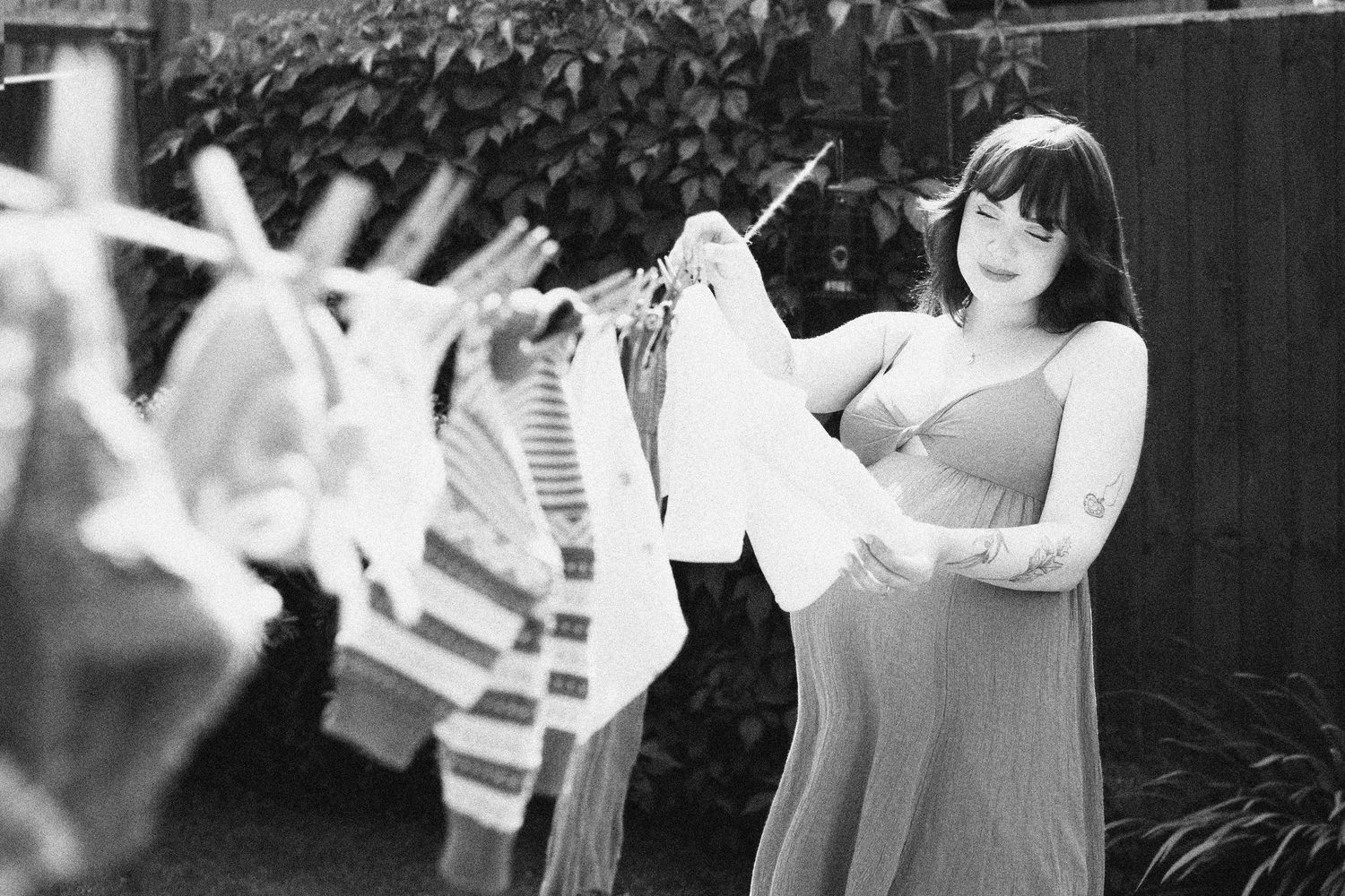 Black and white photo of pregnant woman hanging baby clothes on outdoor clothesline in garden in the West Midlands