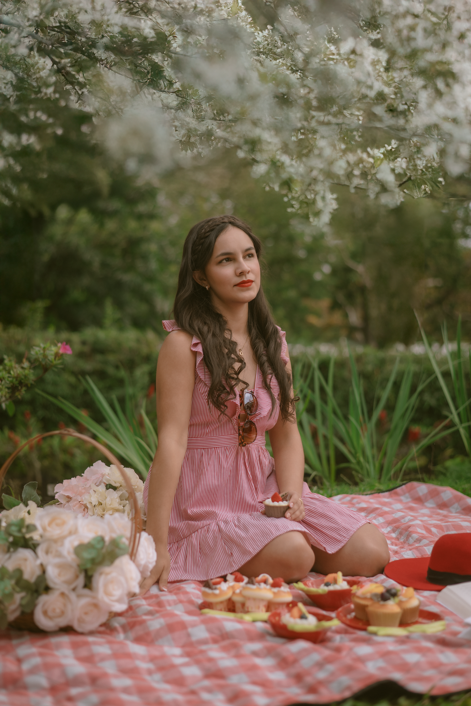A dreamy picnic scene with pink roses and treats laid out on a red checkered blanket in a garden setting.