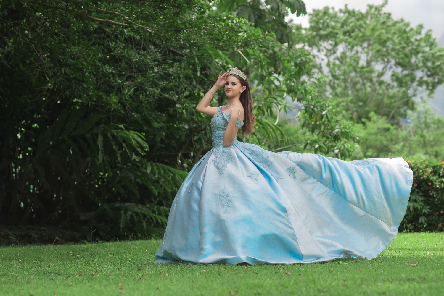 A twirling blue ball gown captured in motion against green garden scenery.