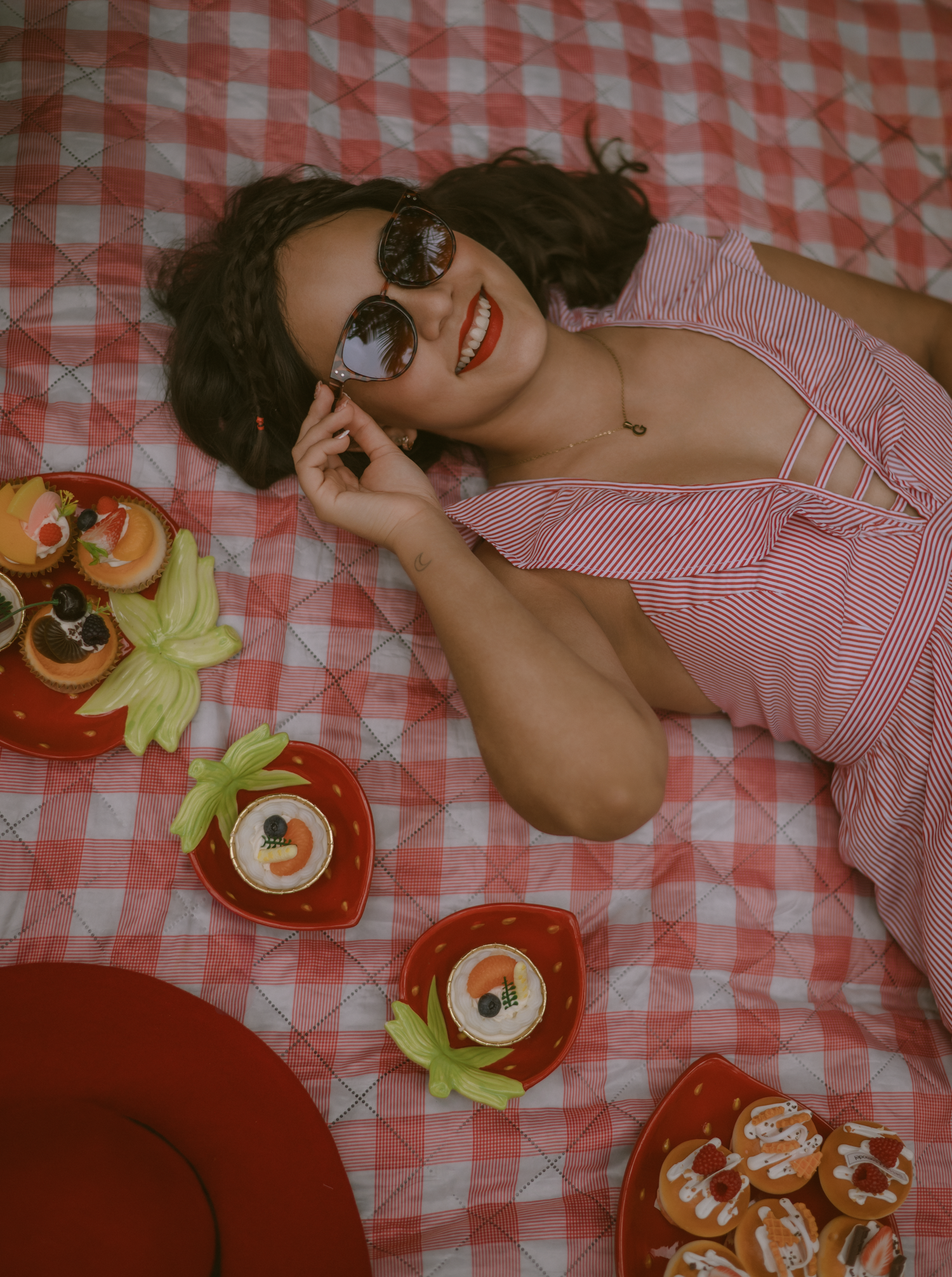 An overhead shot of a picnic setup with pastries and a red hat on a checkered blanket.