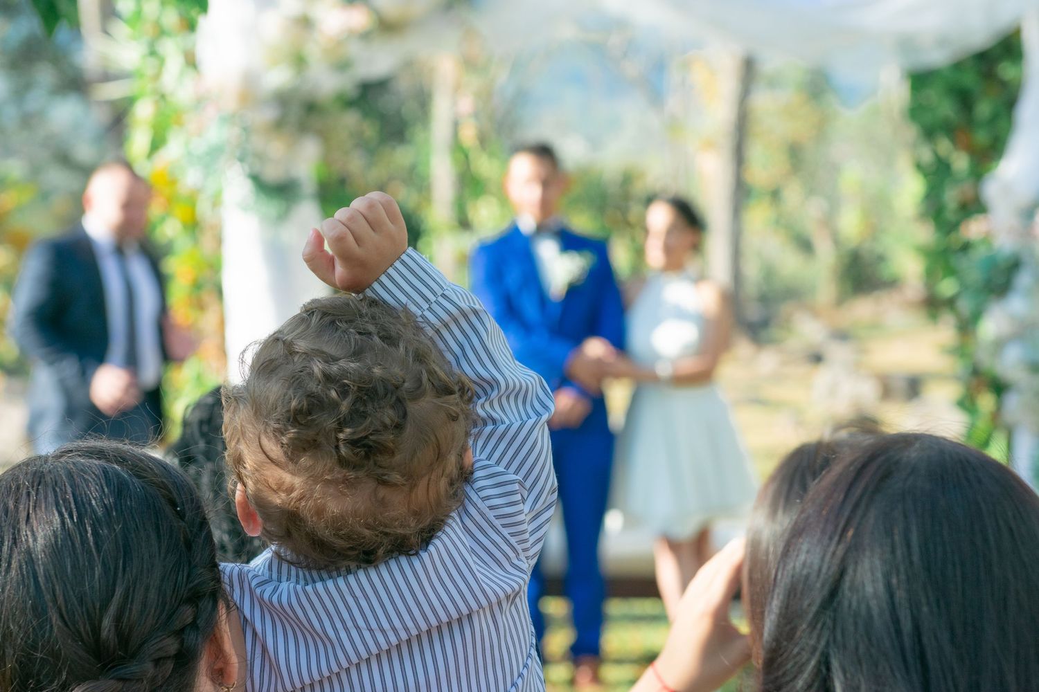 Wedding guests raise their hands in celebration during an outdoor ceremony.