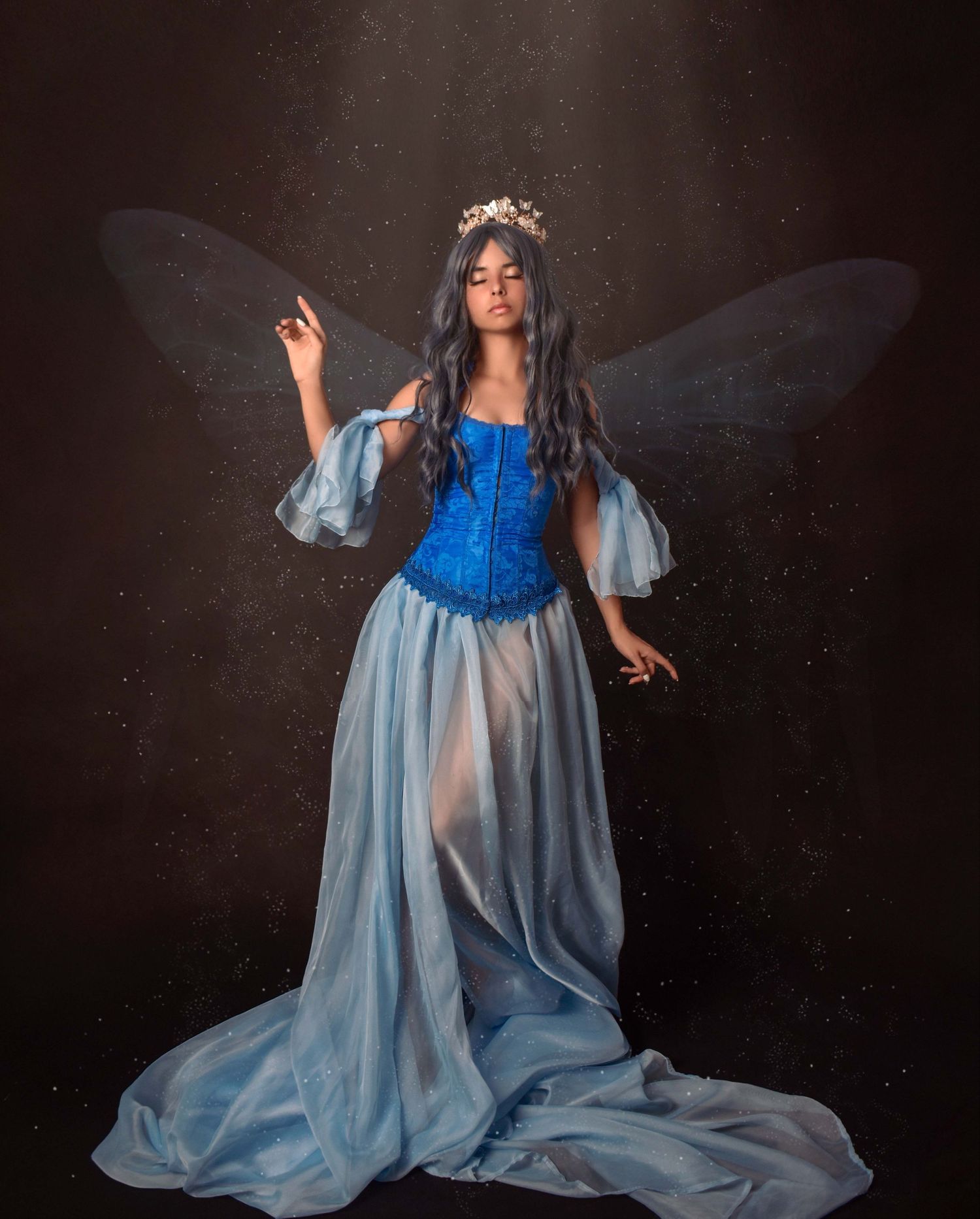 Fantasy portrait featuring ethereal wings and a flowing blue gown in dramatic lighting.