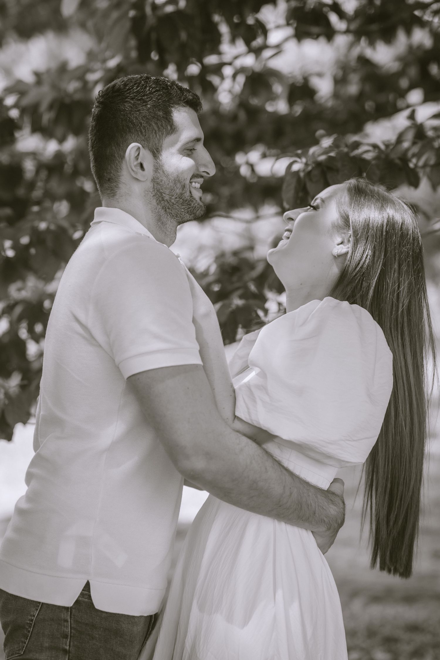 A joyful couple shares a laugh together while embracing in a black and white portrait.