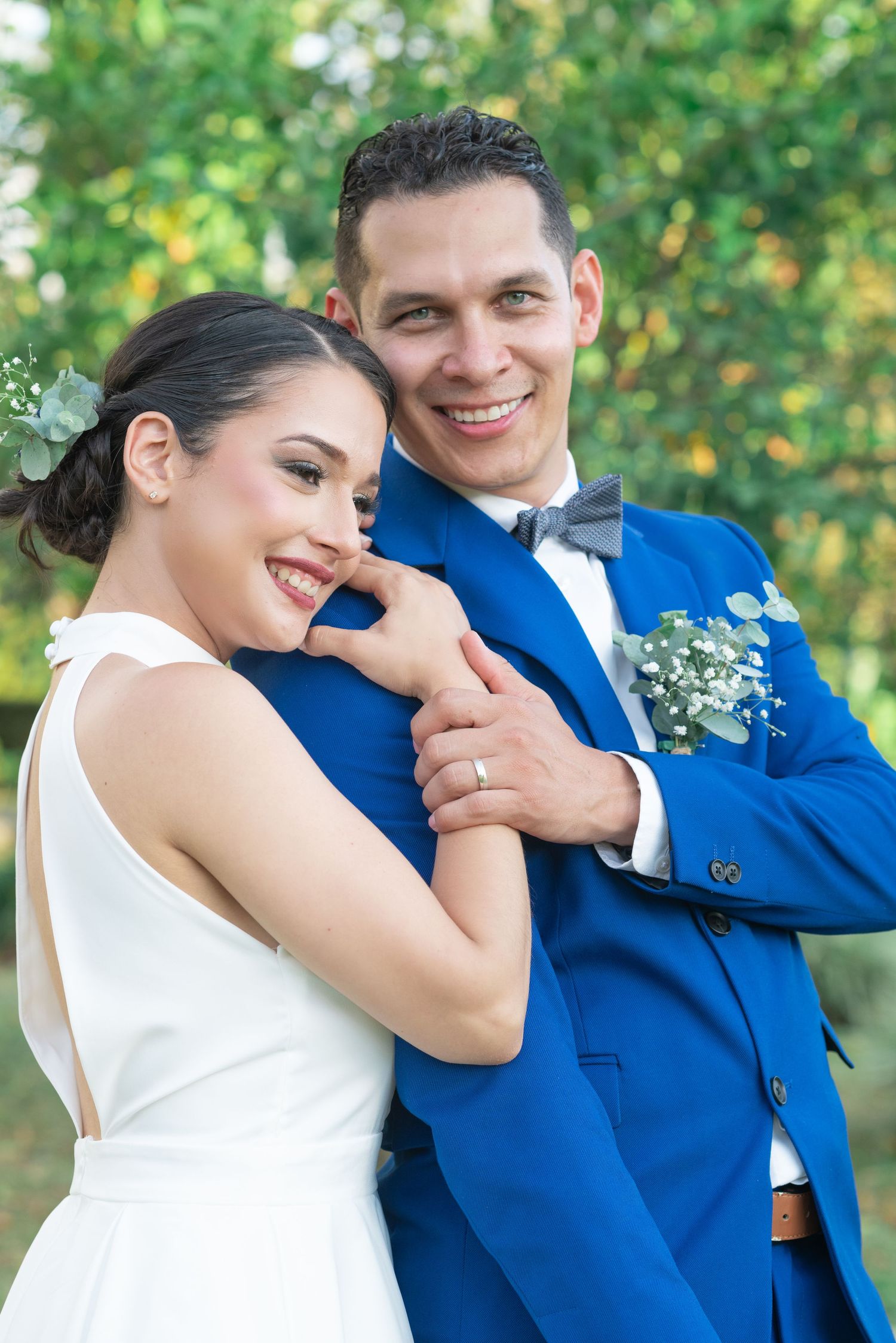 Happy newlyweds embrace outdoors, groom in royal blue suit and bride in sleek white dress.