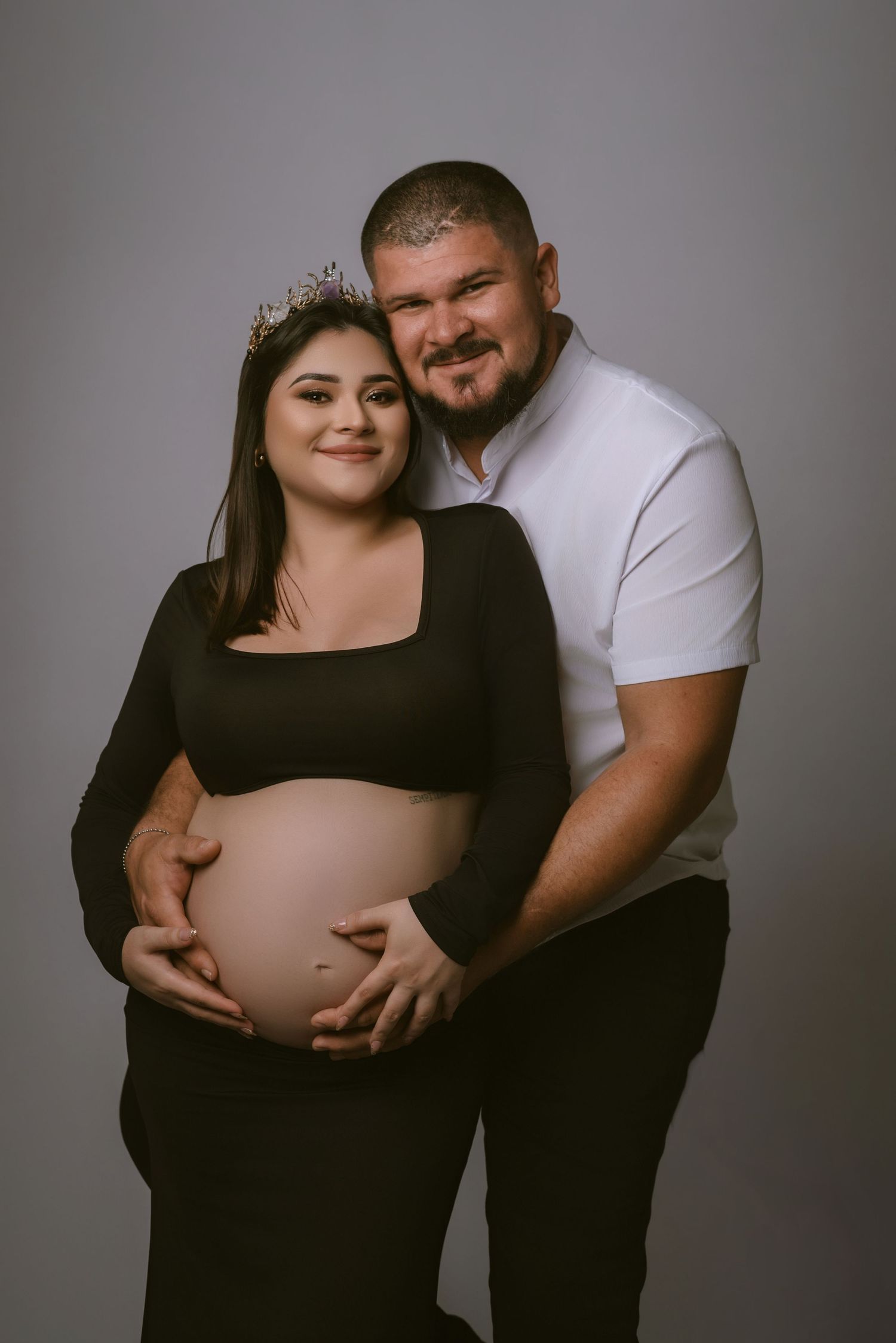 Intimate maternity portrait of expectant couple against grey backdrop.