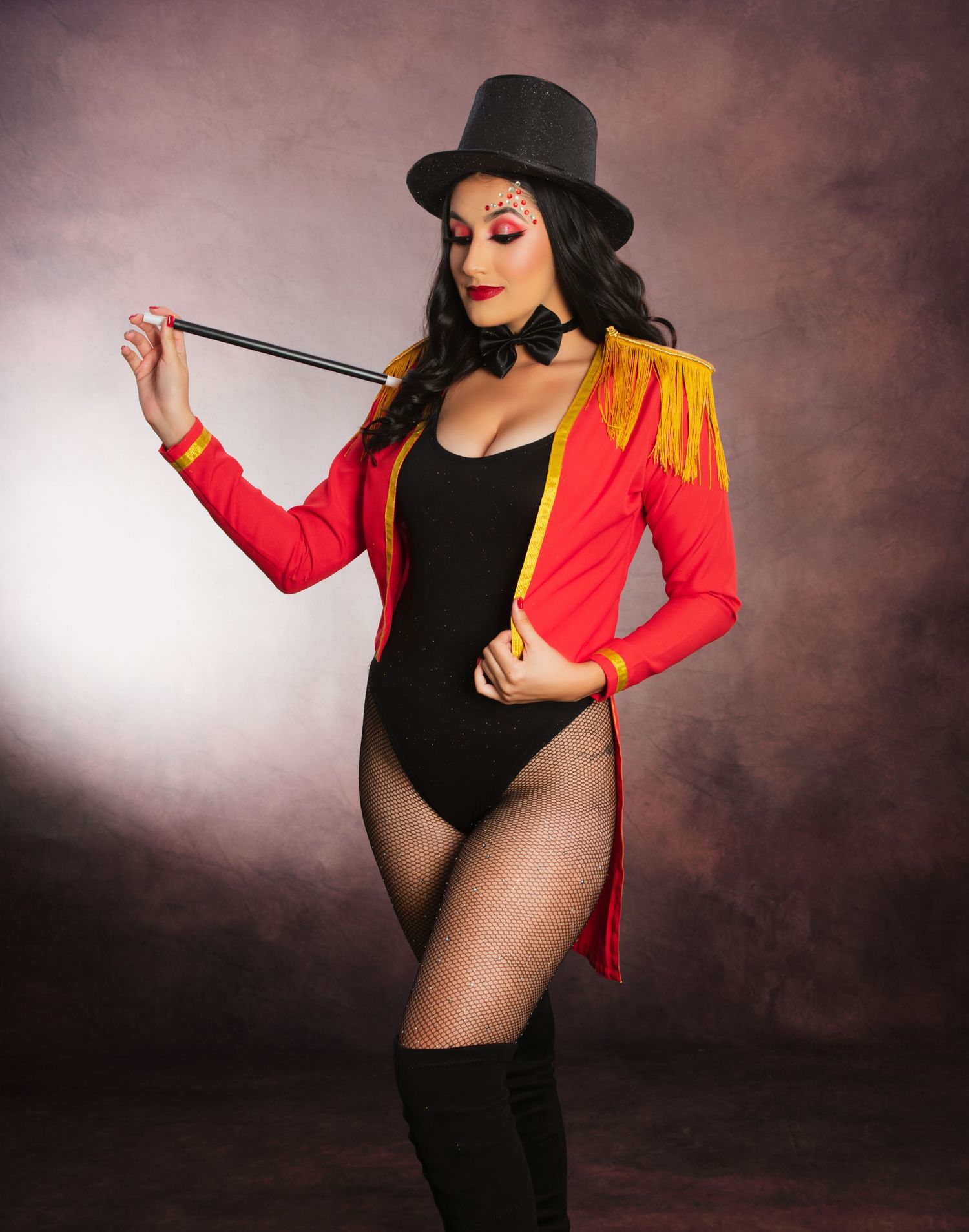 A showgirl poses in a ringmaster costume with top hat and tails against a moody backdrop.
