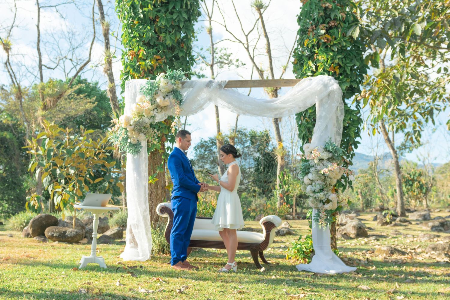 Outdoor wedding ceremony setup with white fabric draped gazebo and floral decorations.