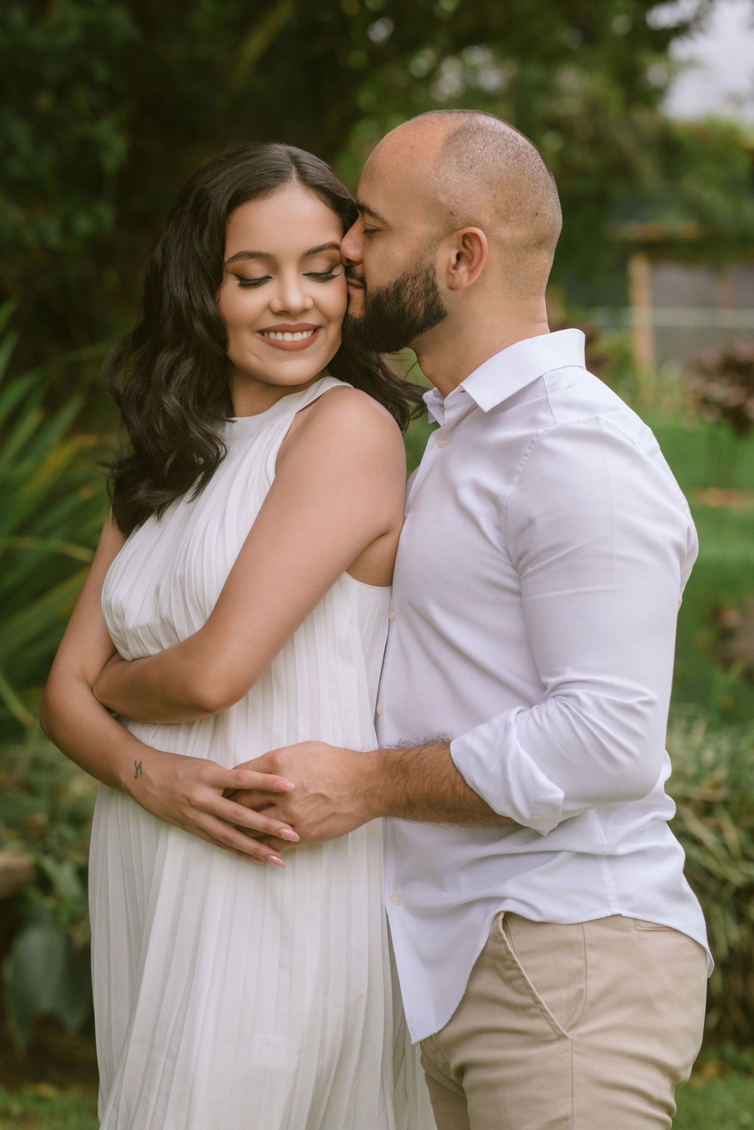 A tender embrace captured in an outdoor garden setting with soft natural lighting.