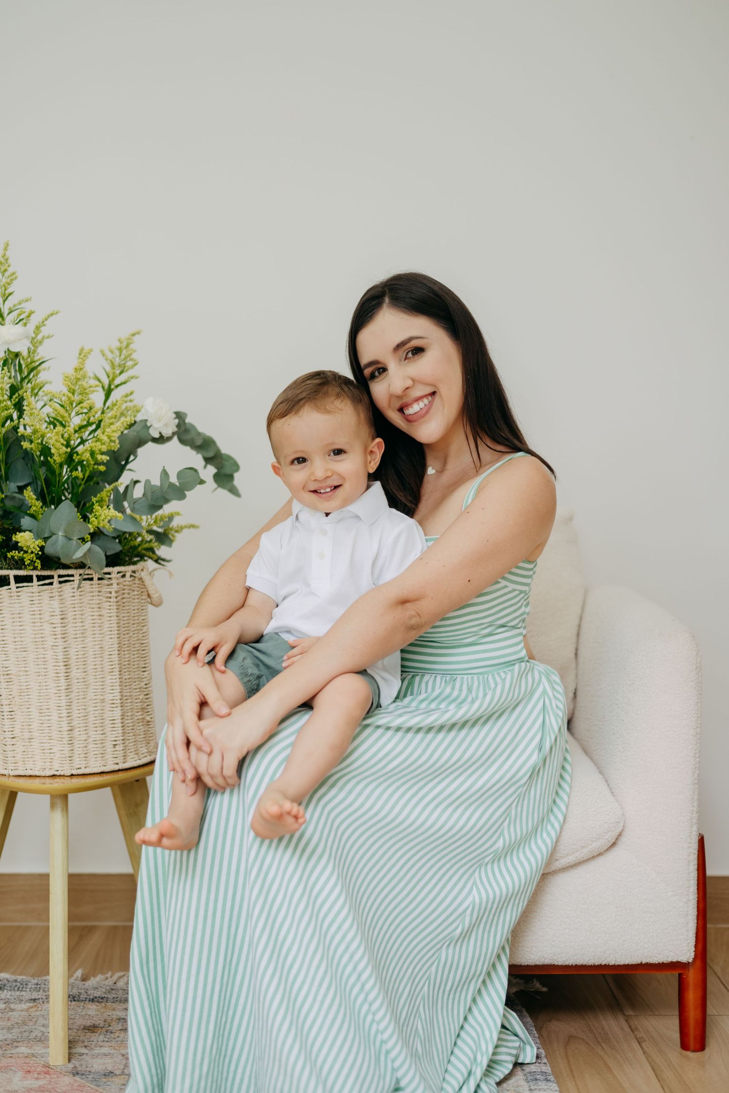 Natural lifestyle portrait in mint striped dress beside woven basket with greenery.